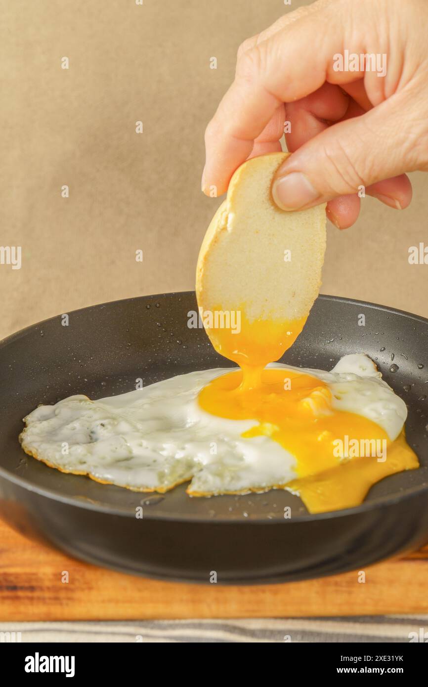 Mano della donna che immerge il pane sul tuorlo di un uovo fritto nell'olio d'oliva Foto Stock