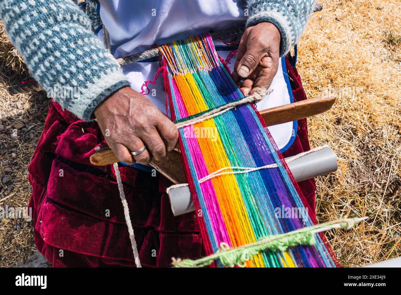 Povera donna adulta indigena artigiana con maschera blu e tipica tessitura ancestrale in tempi di pandemia di covid-19 in una giornata di sole nelle Ande Foto Stock