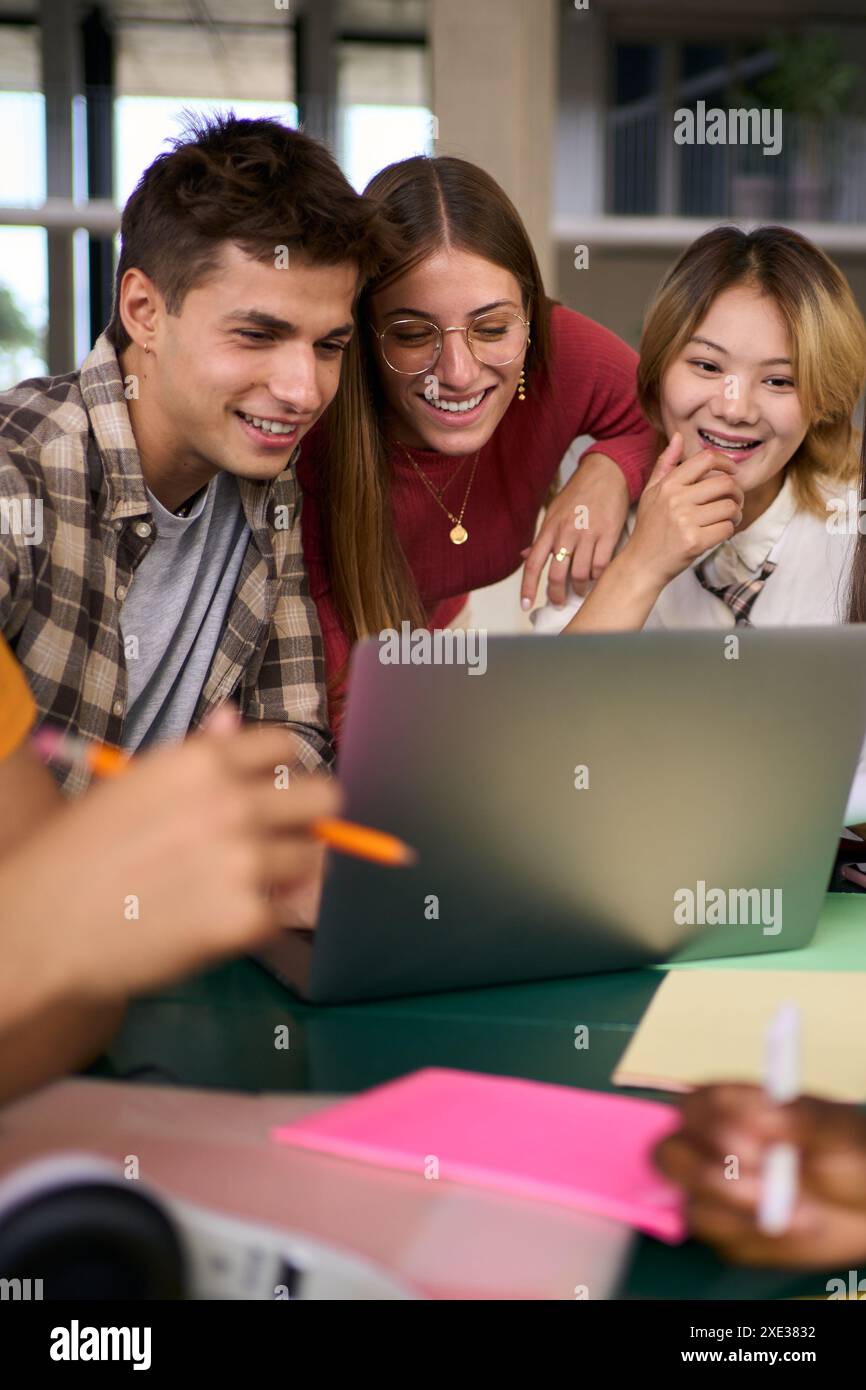 Tre giovani studenti universitari si sono riuniti insieme usando un computer portatile nella sala studi del campus. Foto Stock