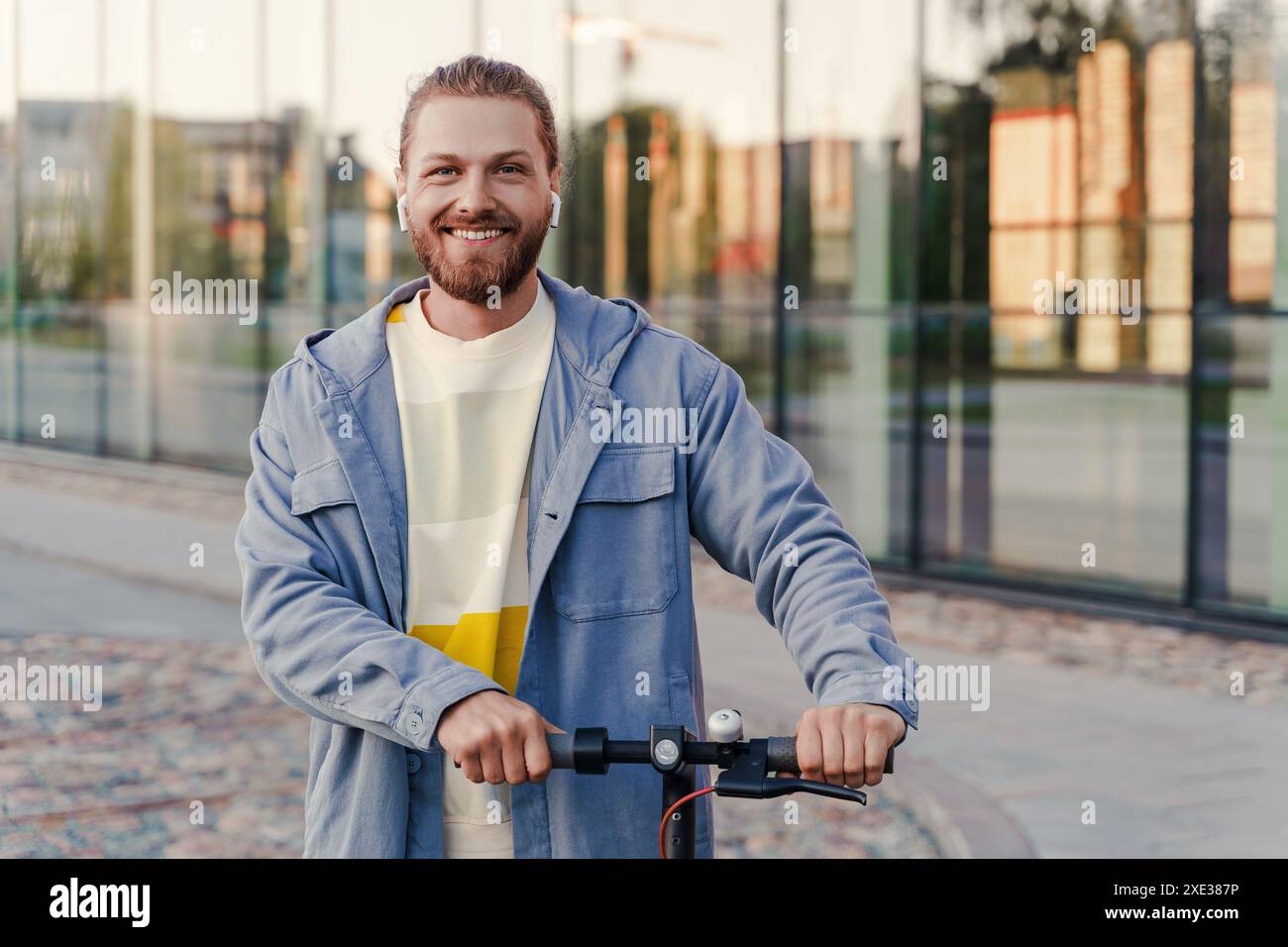 Giovane uomo allegro in sella al suo e-scooter per la strada della città Foto Stock