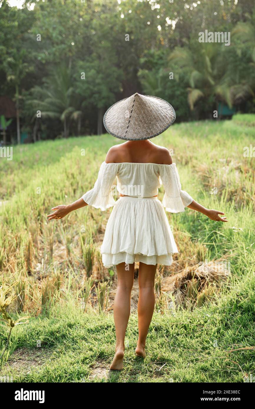 Donna che indossa abiti naturali e cappello conico asiatico nel campo di riso durante il tramonto Foto Stock