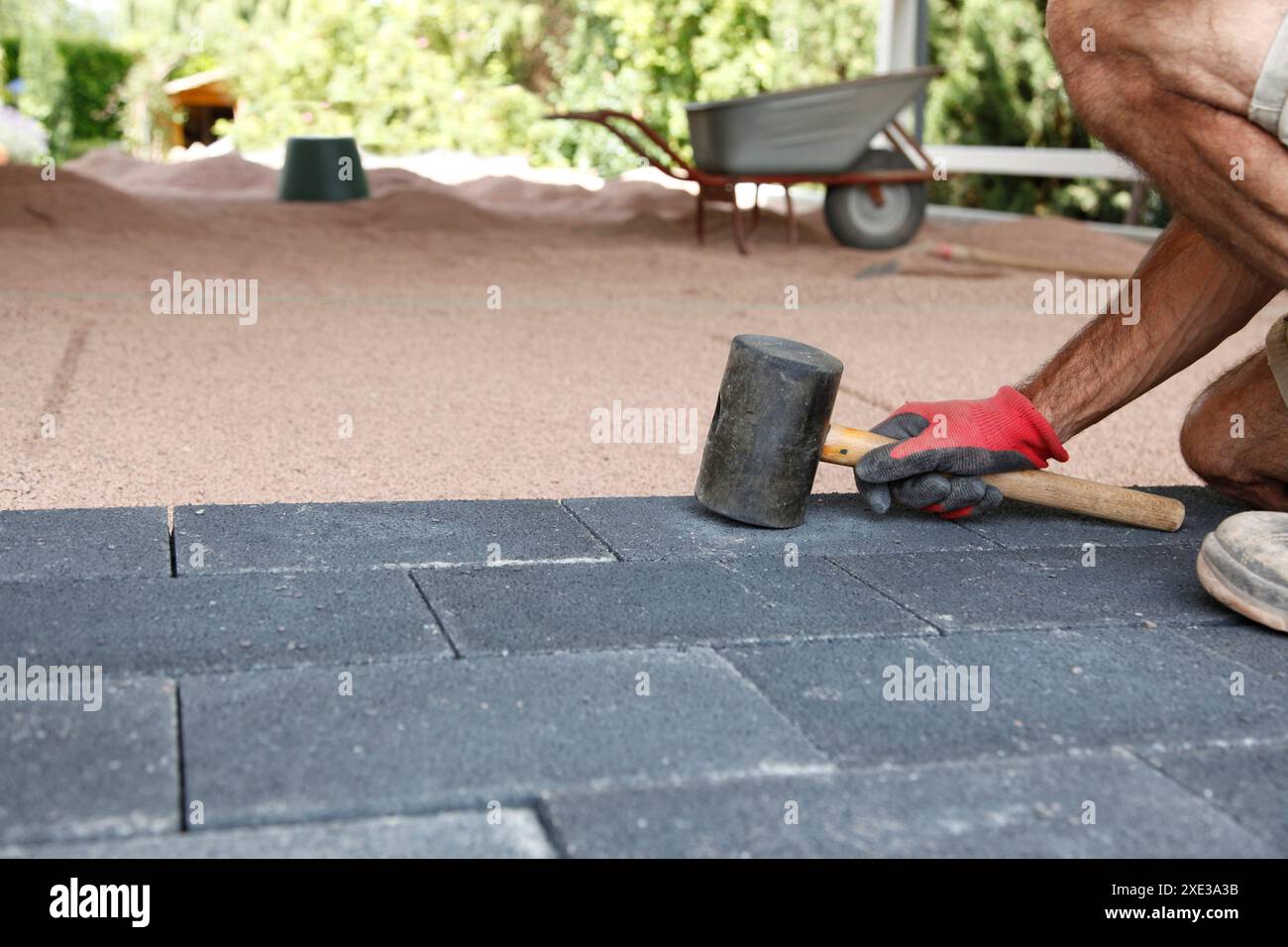 Mani di un lavoratore che posa pavimentazione, grandi blocchi di asfaltatrice per calcestruzzo con martello in mano. Posa di calcestruzzo pav Foto Stock