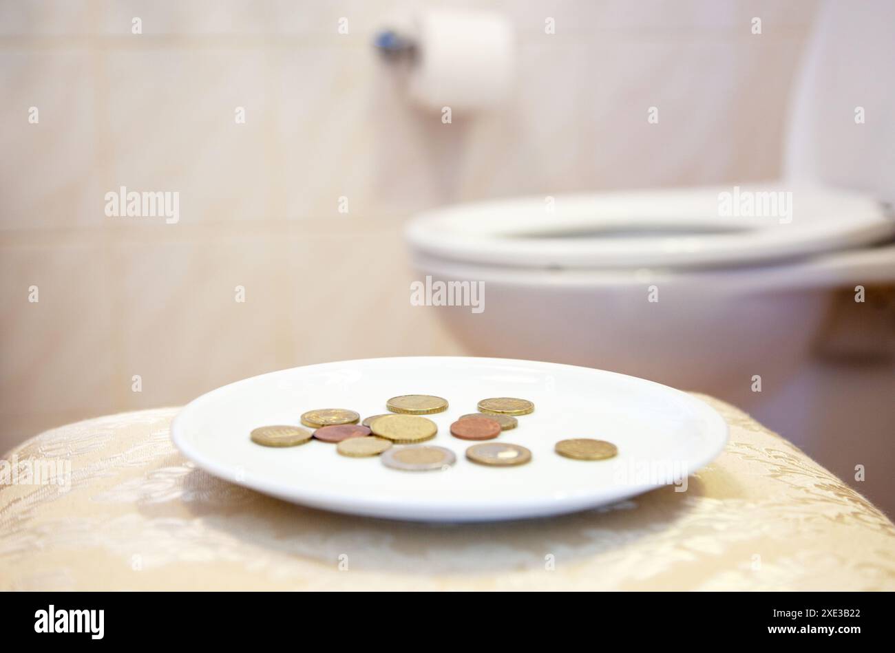Primo piano di monete su Un piatto. Servizi igienici - mancia - a pagamento. Servizi igienici - bagno - WC sullo sfondo. Euro Foto Stock