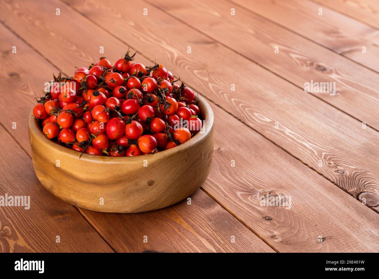 Frutta rosehip rossa di cane-rosa in una ciotola di legno su un tavolo di legno Foto Stock