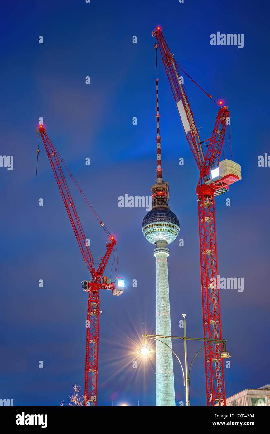 La famosa torre della televisione di Berlino al crepuscolo con due gru rosse Foto Stock