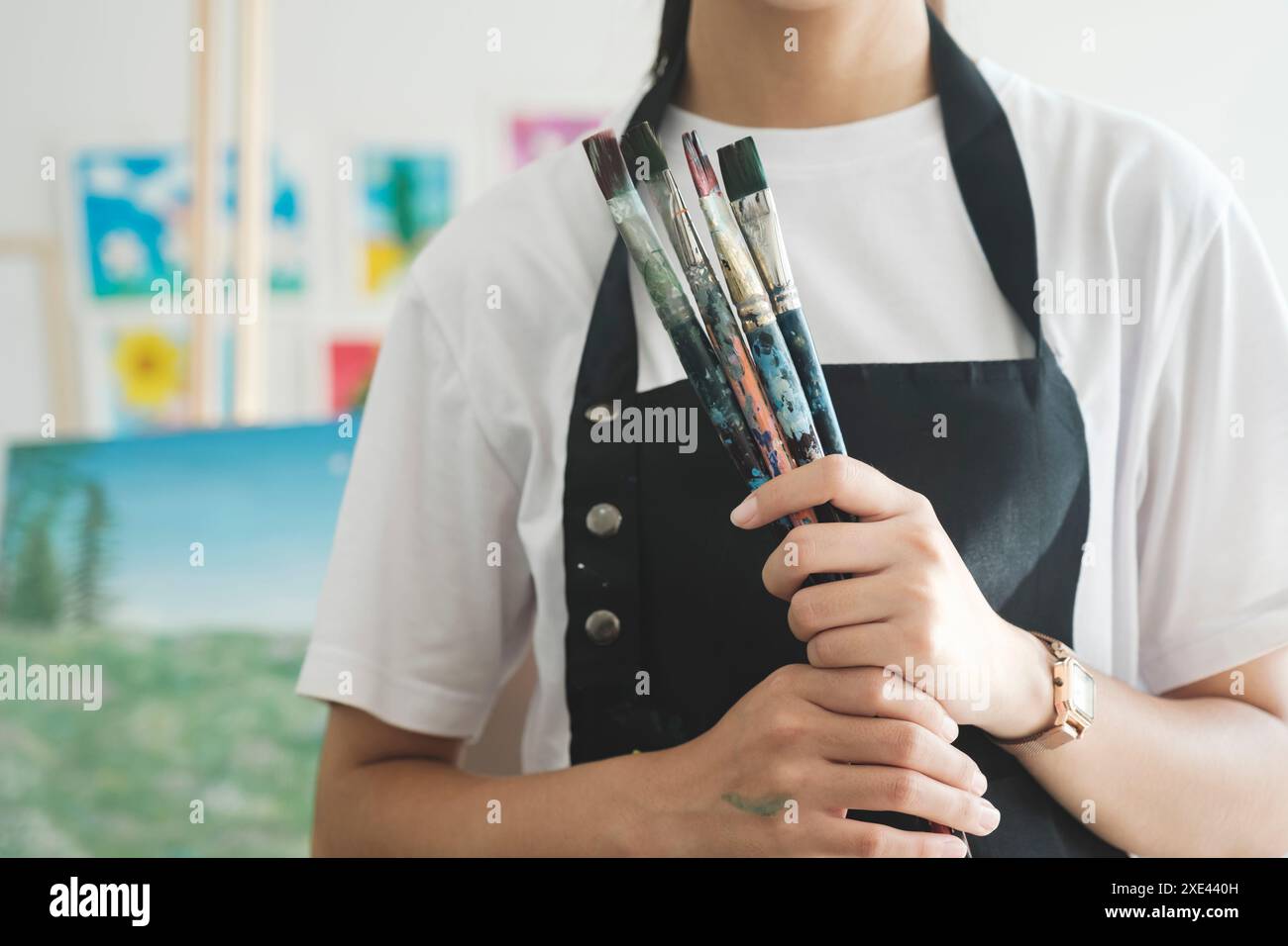 Un primo piano delle mani dell'artista con un grembiule ricoperto di vernice. Frizione di molte spazzole e pennelli. Foto Stock