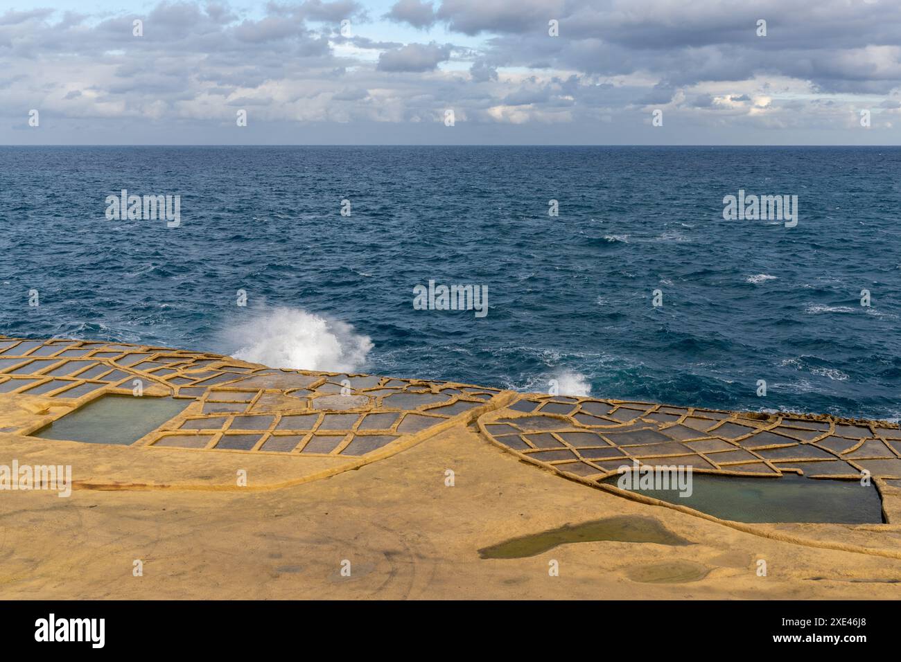 Onde che si infrangono sulla riva presso le saline della baia di Xwejni Foto Stock