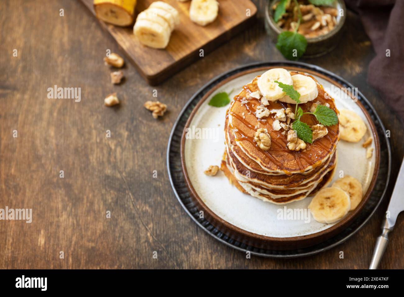 Festeggiamo la giornata dei pancake, colazione all'americana. Deliziose frittelle di banana fatte in casa con noci e caramello su un rustico tavolo in legno. Co Foto Stock