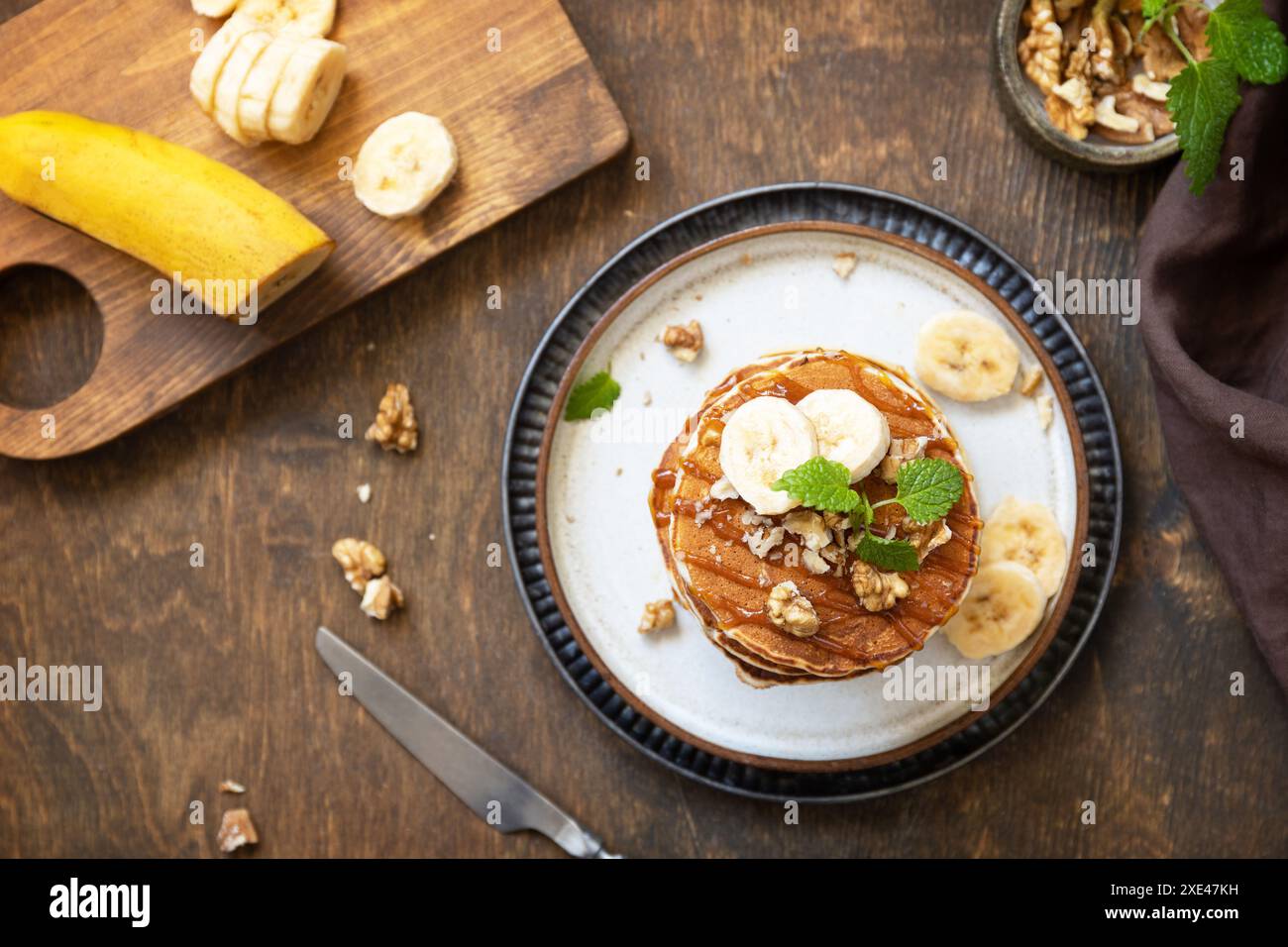 Festeggiamo la giornata dei pancake, colazione all'americana. Deliziose frittelle di banana fatte in casa con noci e caramello su un rustico tavolo in legno. A. Foto Stock