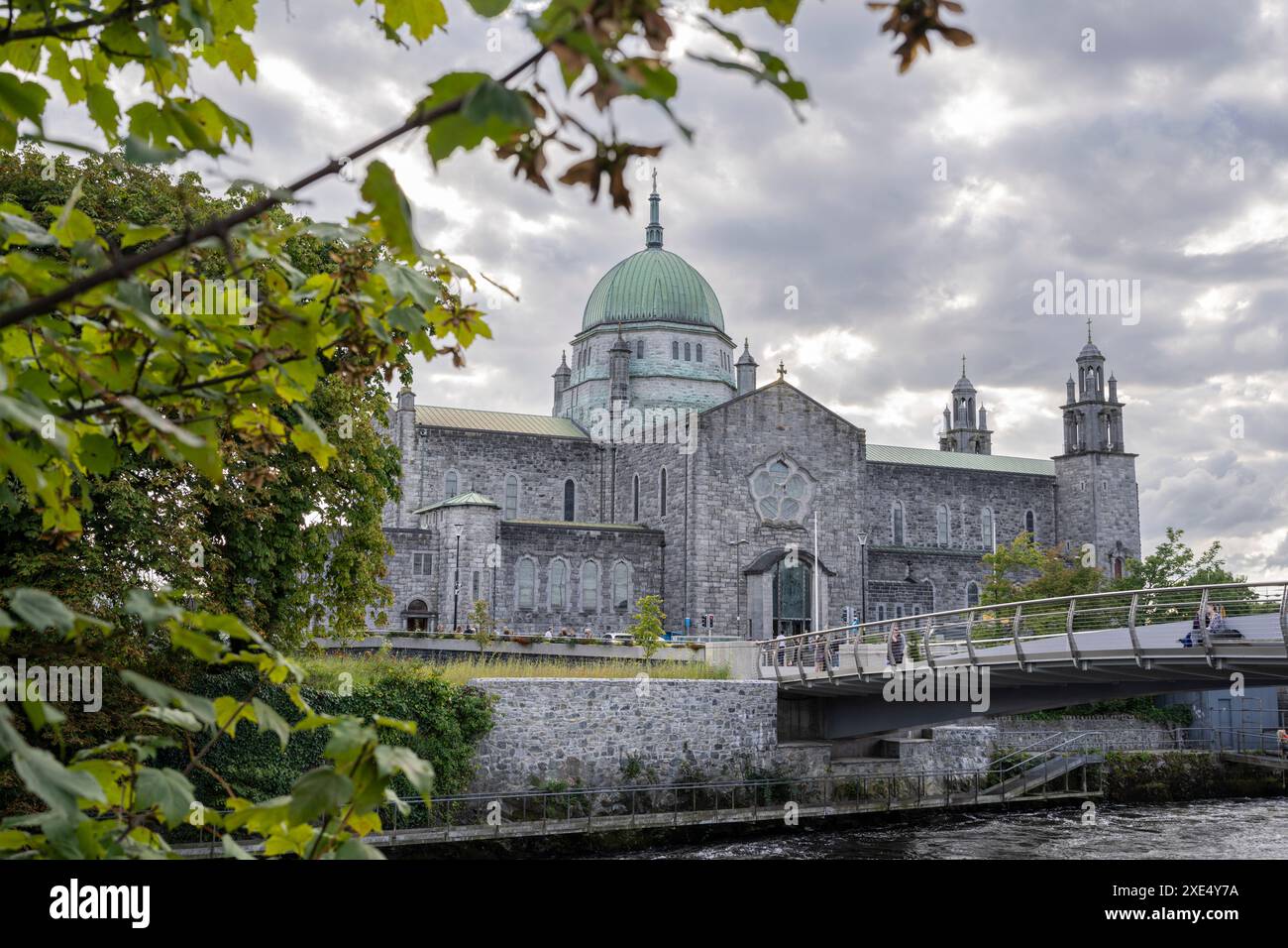 Persone che camminano lungo il fiume Corrib con la cattedrale sullo sfondo Foto Stock