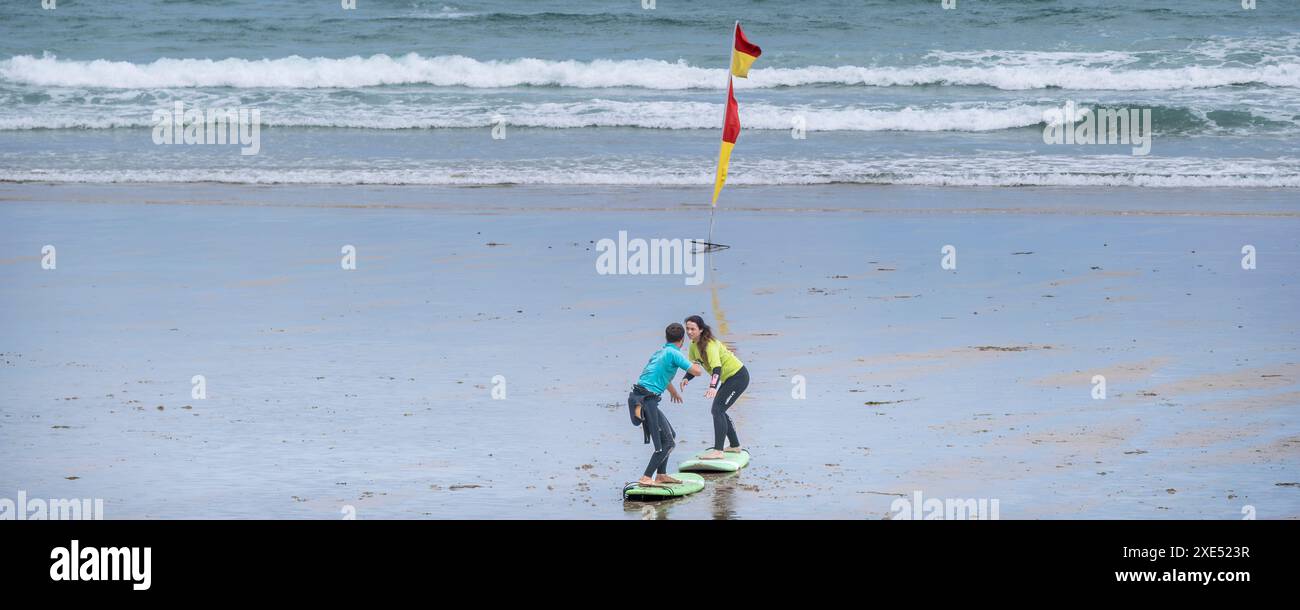 Un'immagine panoramica di un allenatore di surf della Escape Surf School e di un principiante di surf che ha una lezione di surf uno a uno sulla spiaggia di Towan a Newquay in Foto Stock
