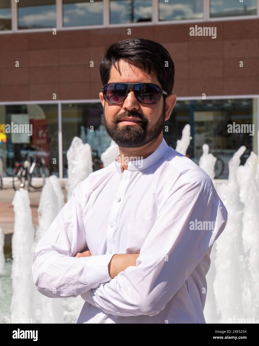 Ritratto ravvicinato di un moderno pakistano con barba scura, vestiti chiari e occhiali da sole Foto Stock