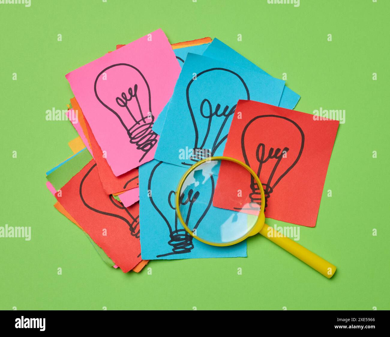 Lampadine disegnate su fogli di carta e una lente d'ingrandimento in plastica, il concetto di ricerca di nuove idee. Foto Stock
