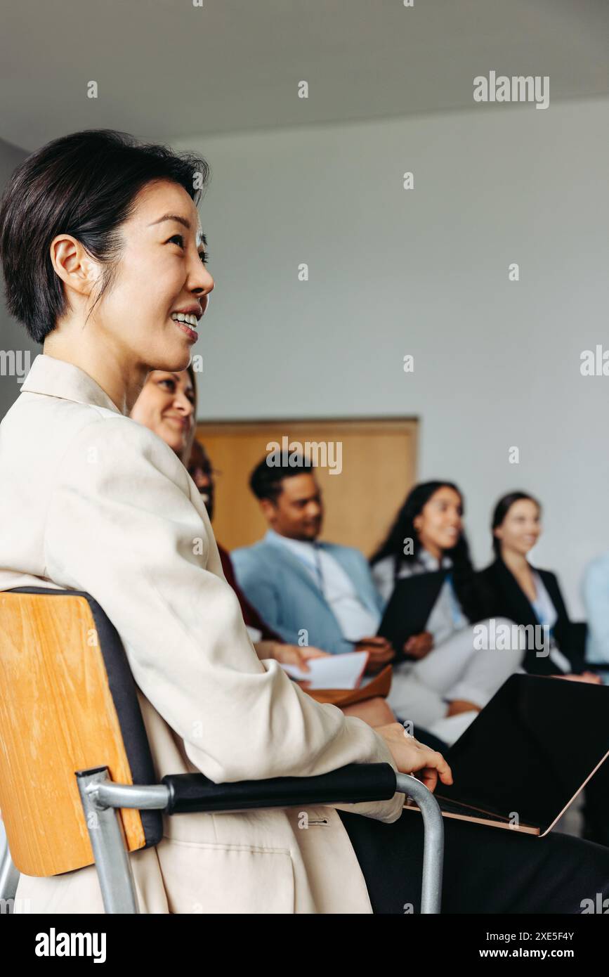 Imprenditrice di successo di etnia asiatica sorridente durante un incontro d'affari insieme ai colleghi, trasmettendo lavoro di squadra e fiducia. Foto Stock