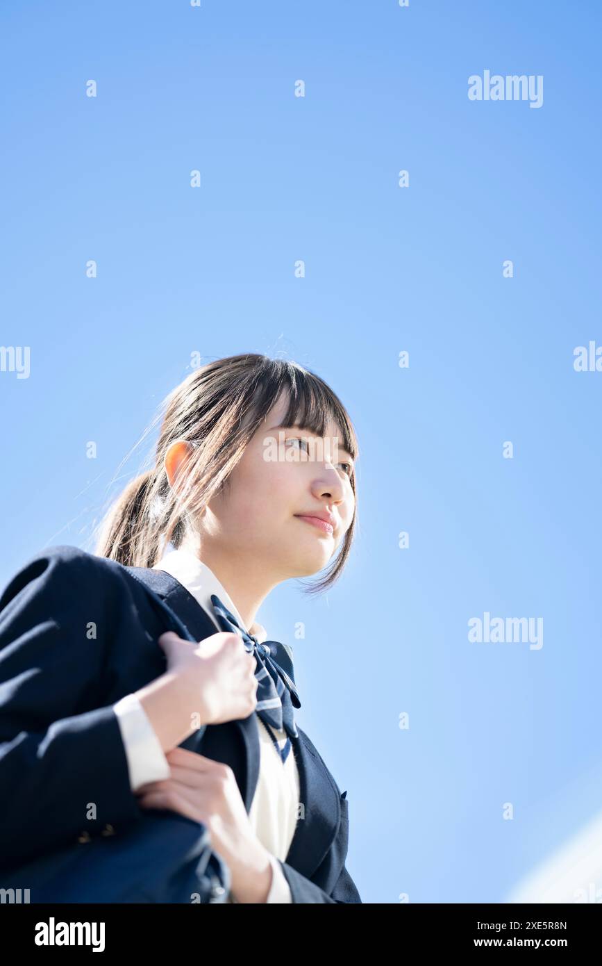 Studentessa in uniforme che guarda in lontananza con il cielo blu sullo sfondo Foto Stock