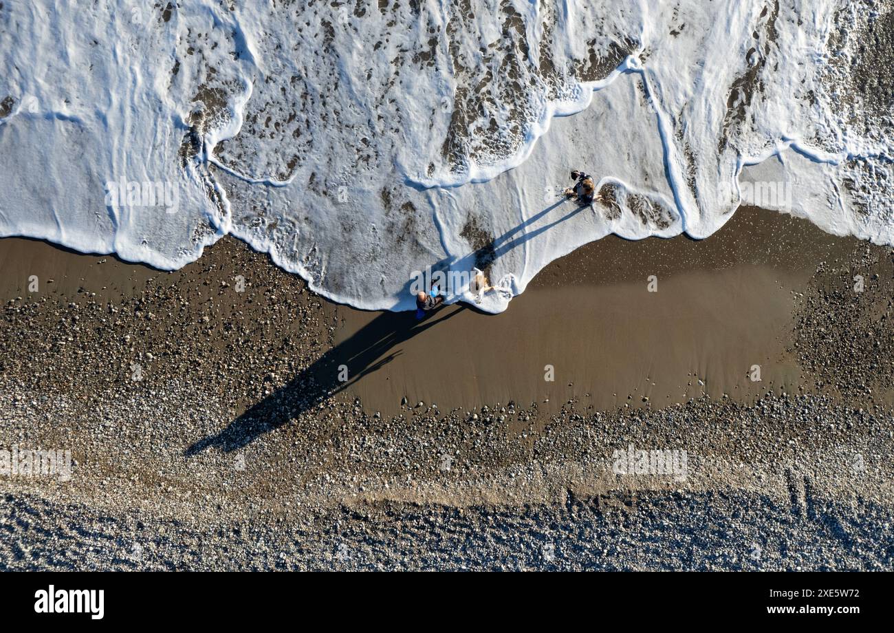 Scenario aereo con droni di persone che camminano sulla sabbia in una spiaggia. Onde tempestose spiaggia idilliaca in inverno Foto Stock