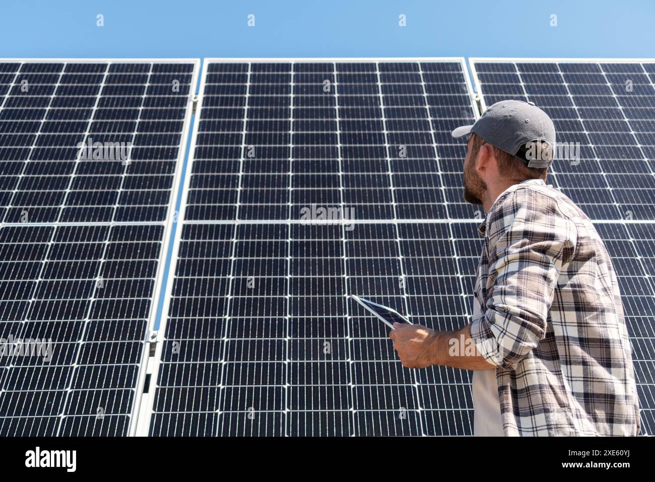 Manutenzione di stazioni solari. Foto ad angolo basso di un lavoratore di una centrale solare che tiene in mano un tablet digitale che guarda un pannello solare. Foto Stock