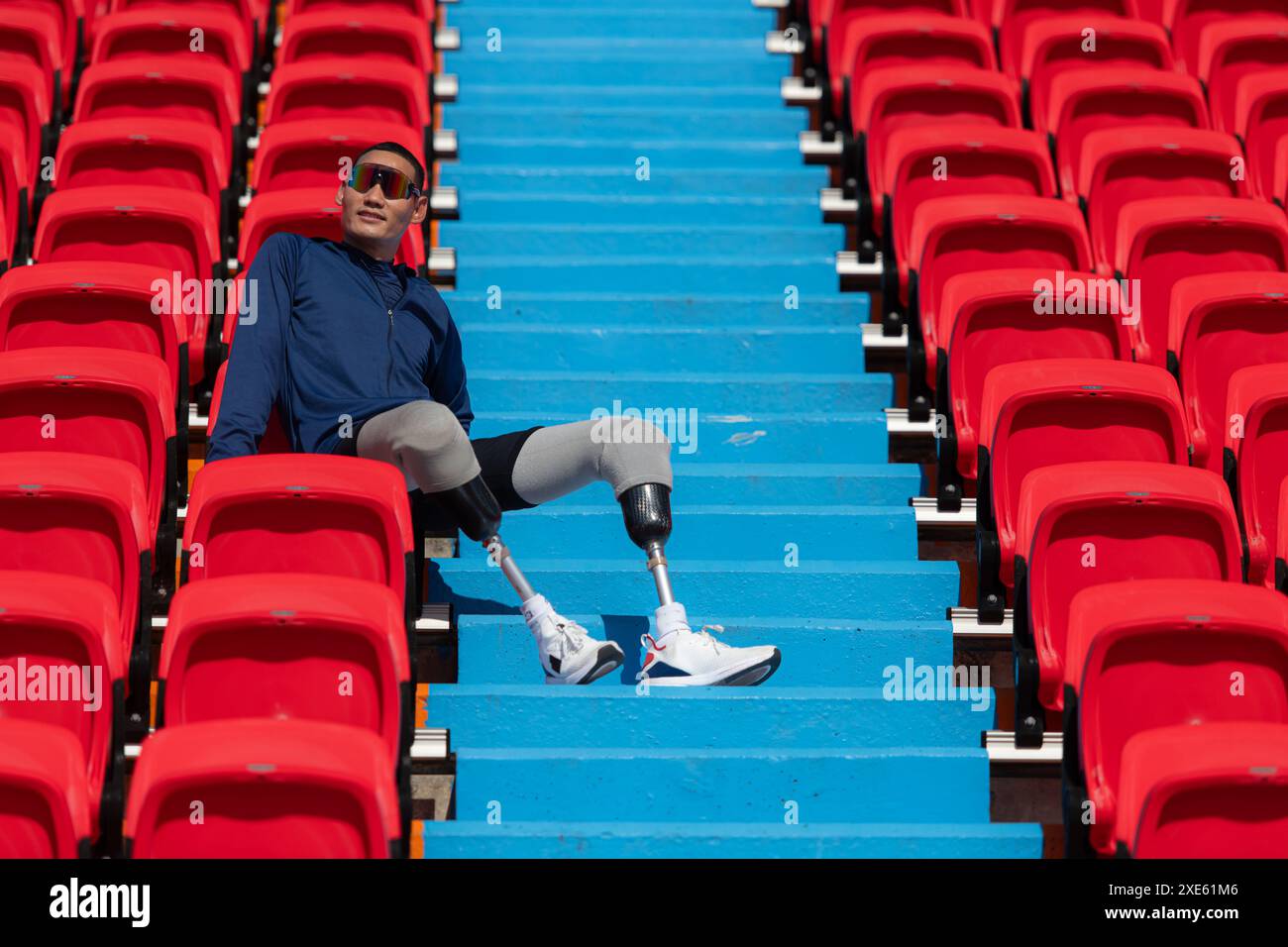 Gli atleti disabili con una camicia blu seduti sui sedili rossi dello stadio, si preparano per l'allenamento di corsa. Foto Stock