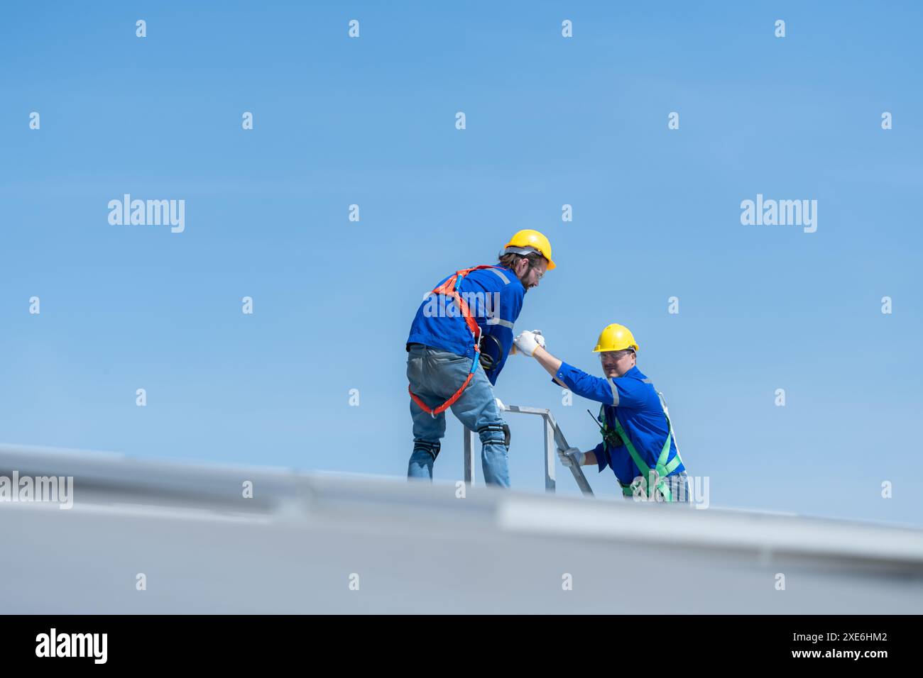 Un giovane tecnico tirocinante che lavora sui pannelli solari teme le altezze con ingegneri senior che aiutano sempre Foto Stock