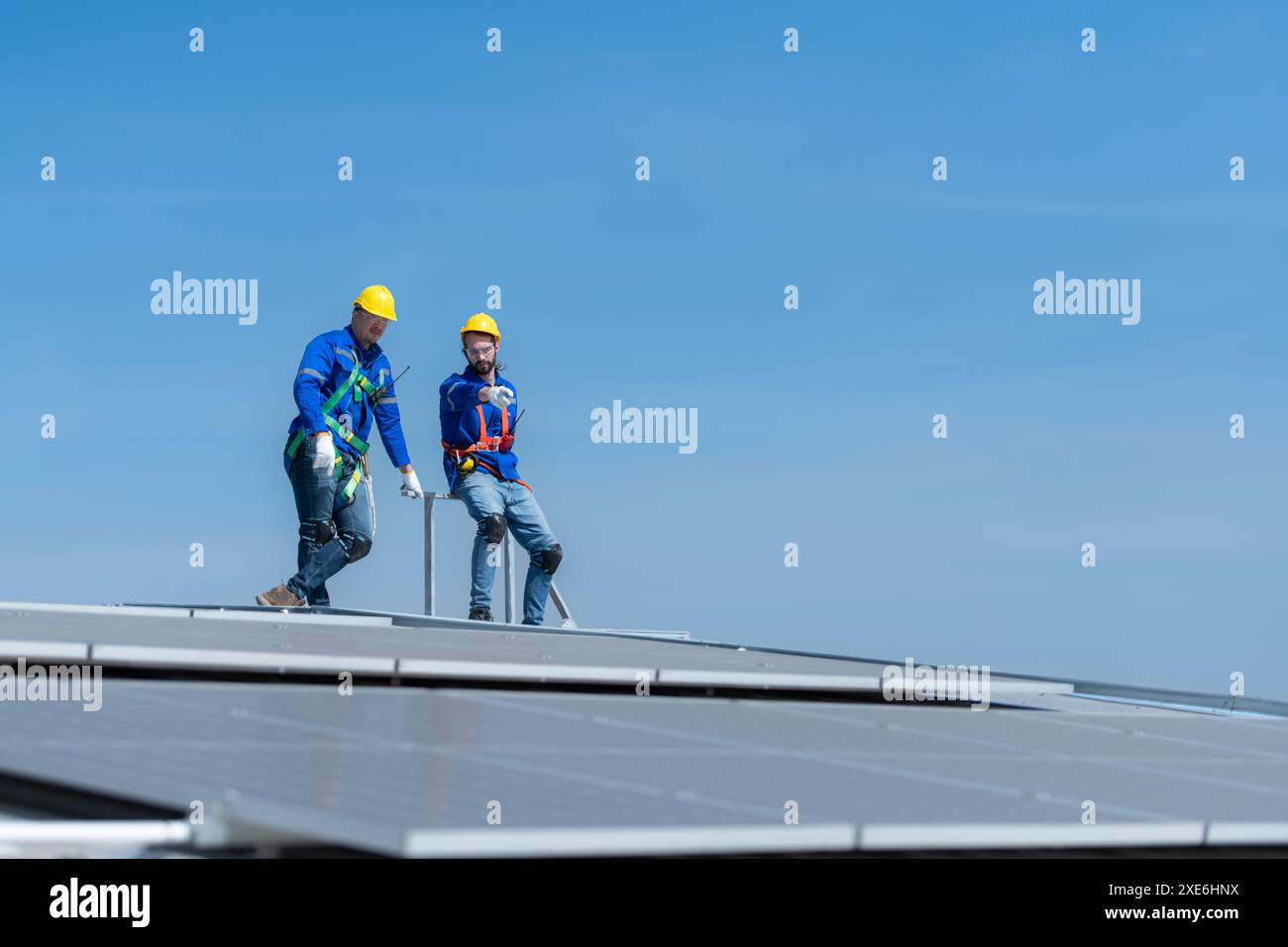 Un giovane tecnico tirocinante che lavora sui pannelli solari teme le altezze con ingegneri senior che aiutano sempre Foto Stock