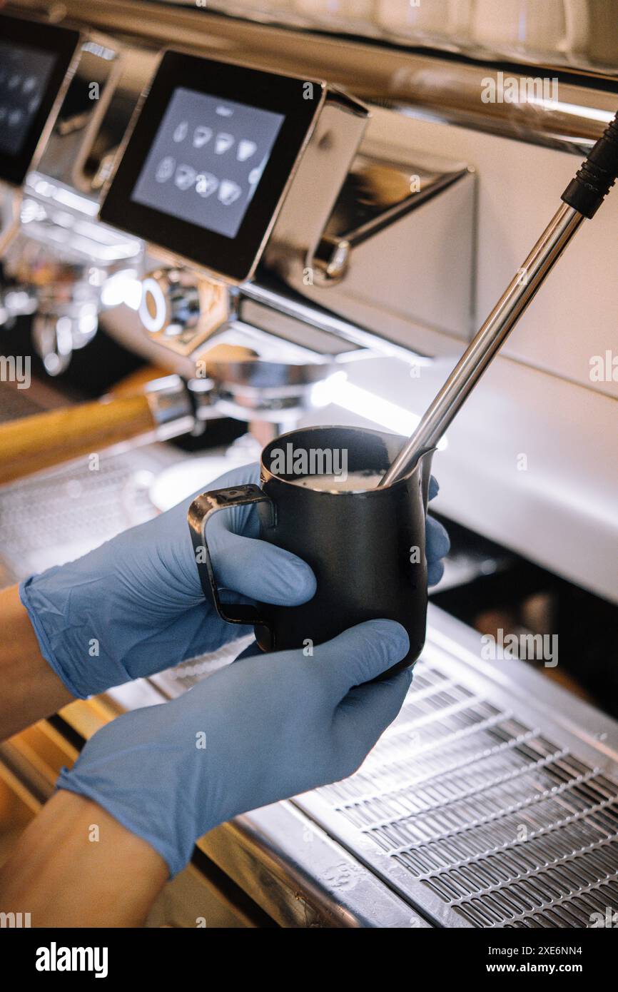 Il barista prepara la schiuma di latte nella tazza metallica Foto Stock
