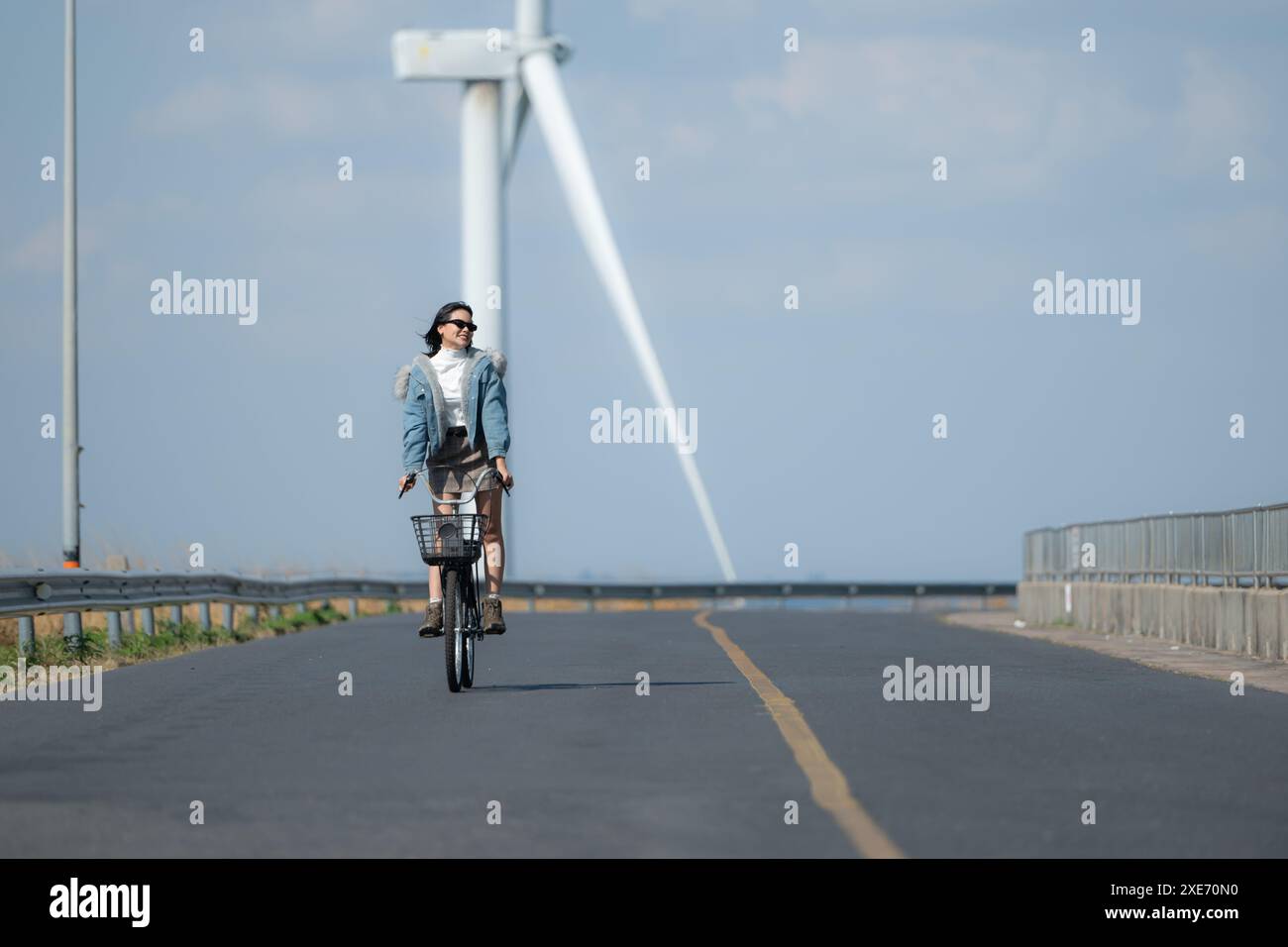 Giovane donna in bicicletta su una strada in un mulino a vento. Foto Stock