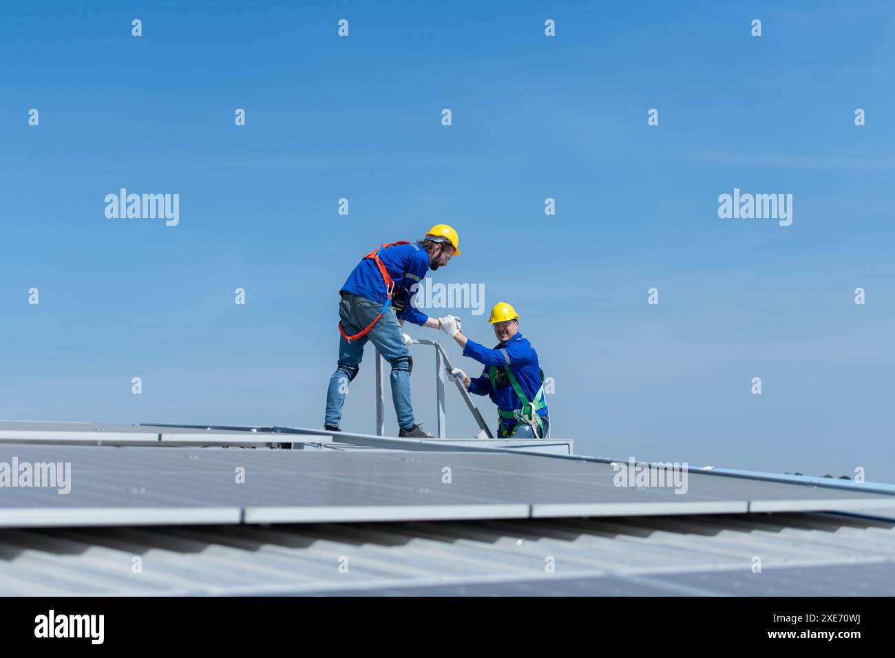 Un giovane tecnico tirocinante che lavora sui pannelli solari teme le altezze con ingegneri senior che aiutano sempre Foto Stock