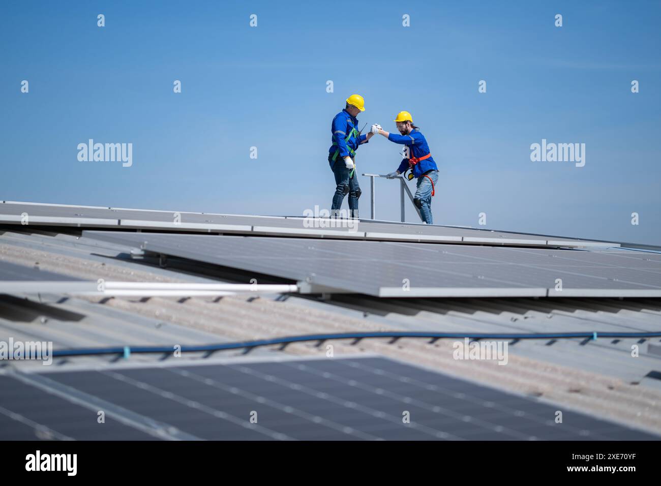 Un giovane tecnico tirocinante che lavora sui pannelli solari teme le altezze con ingegneri senior che aiutano sempre Foto Stock