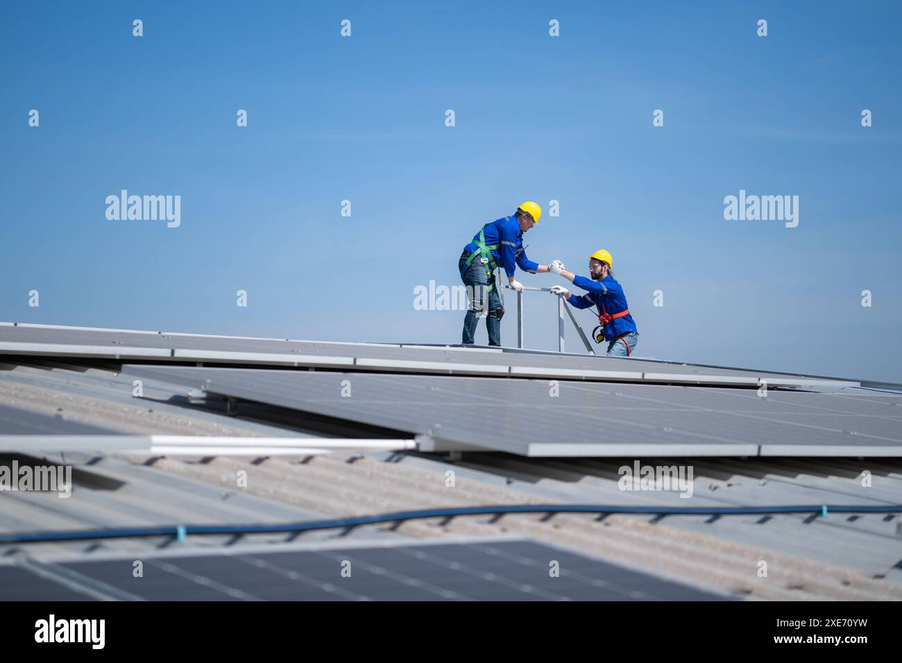 Un giovane tecnico tirocinante che lavora sui pannelli solari teme le altezze con ingegneri senior che aiutano sempre Foto Stock