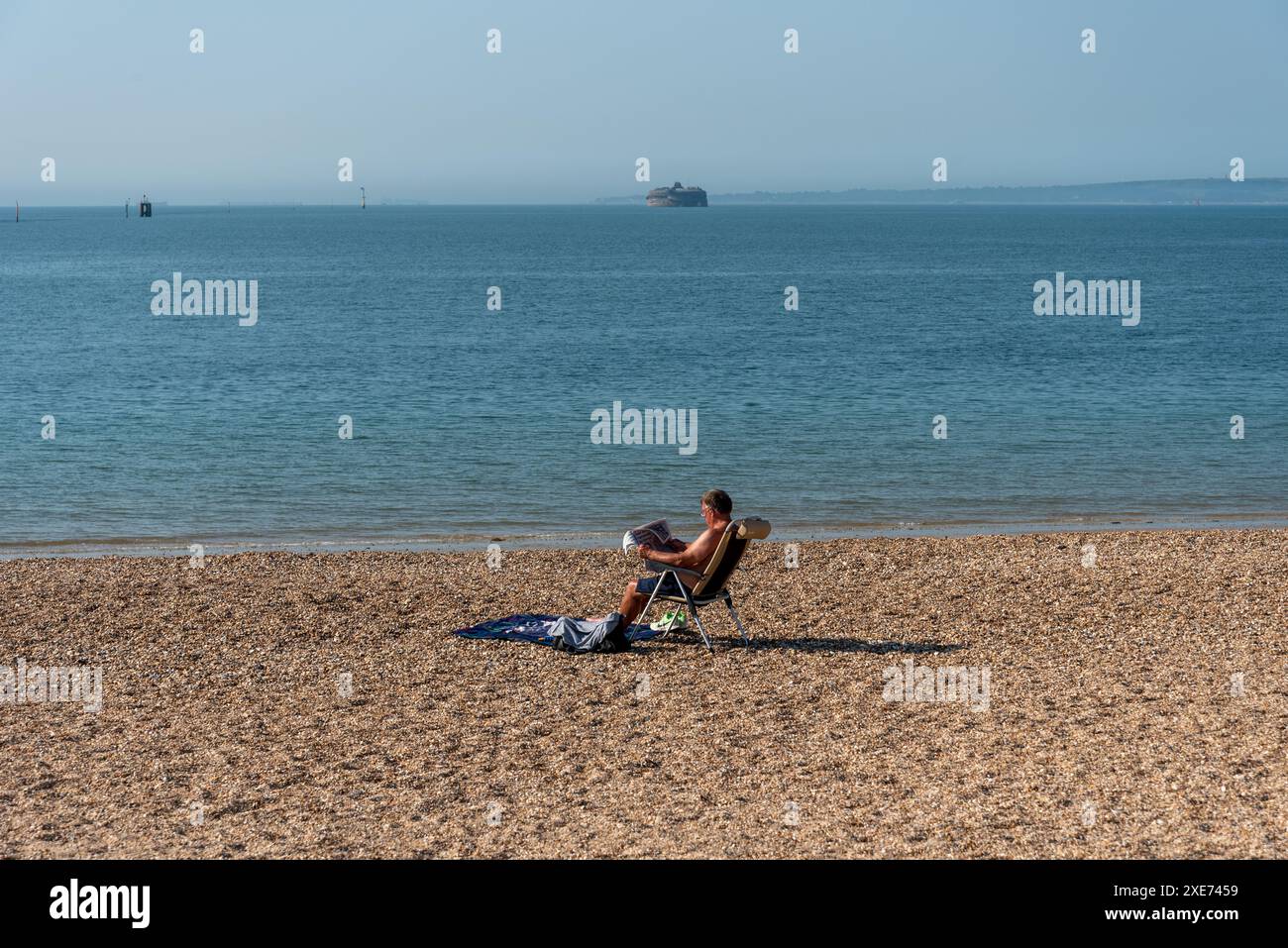 Un uomo siede su una spiaggia da solo a leggere un giornale al sole estivo. Foto Stock