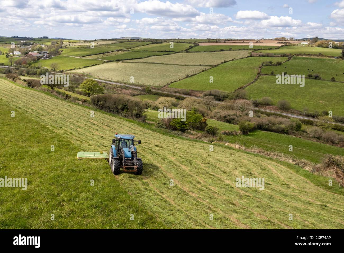 Un agricoltore taglia l'insilato con un trattore New Holland e un rasaerba Krone R240 a Knocknageehy, West Cork, Irlanda. Foto Stock