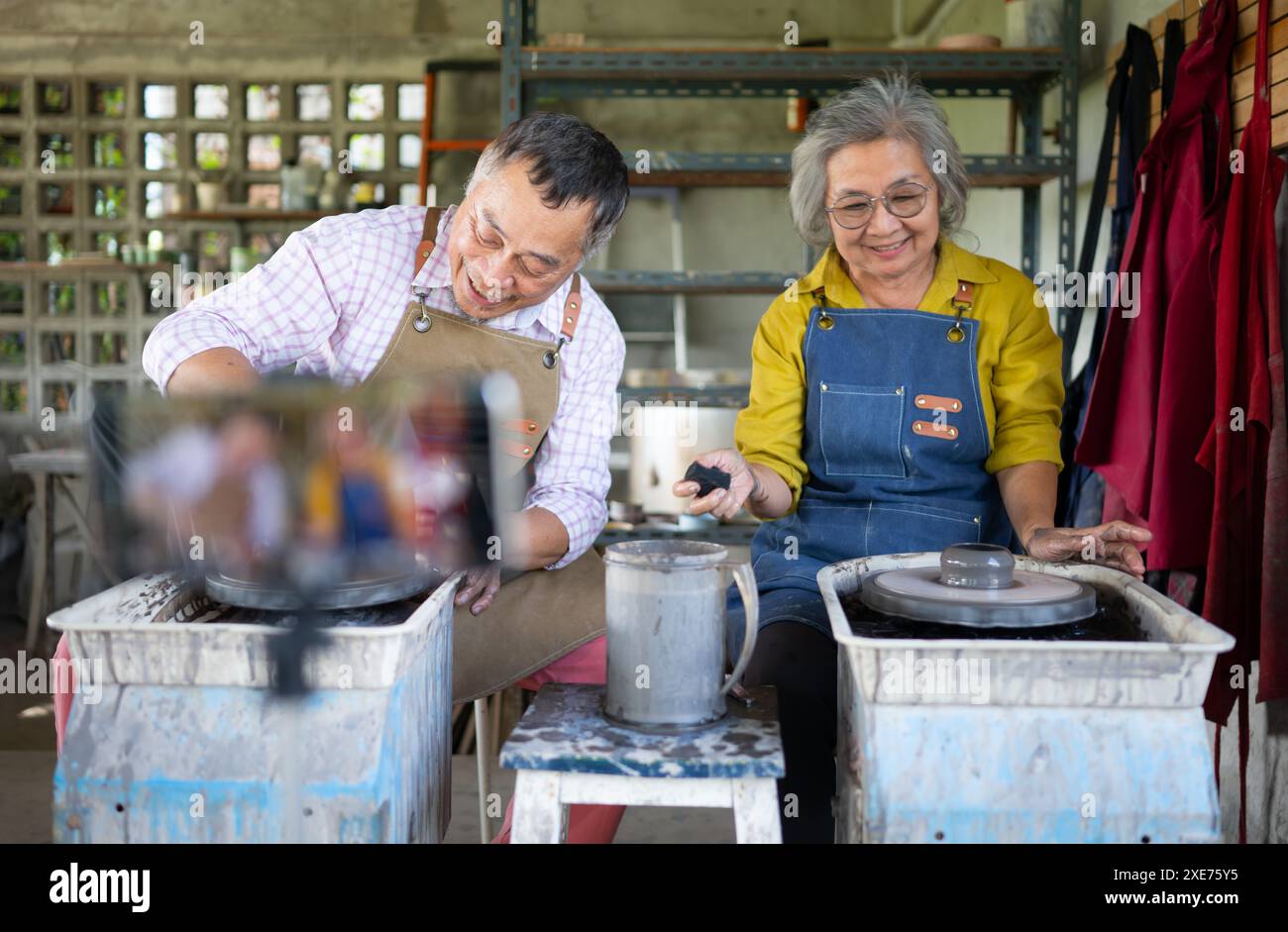 Coppia asiatica in pensione con attività di produzione di ceramiche e pittura di argilla nel laboratorio di ceramica con trasmissione dal vivo via social Foto Stock