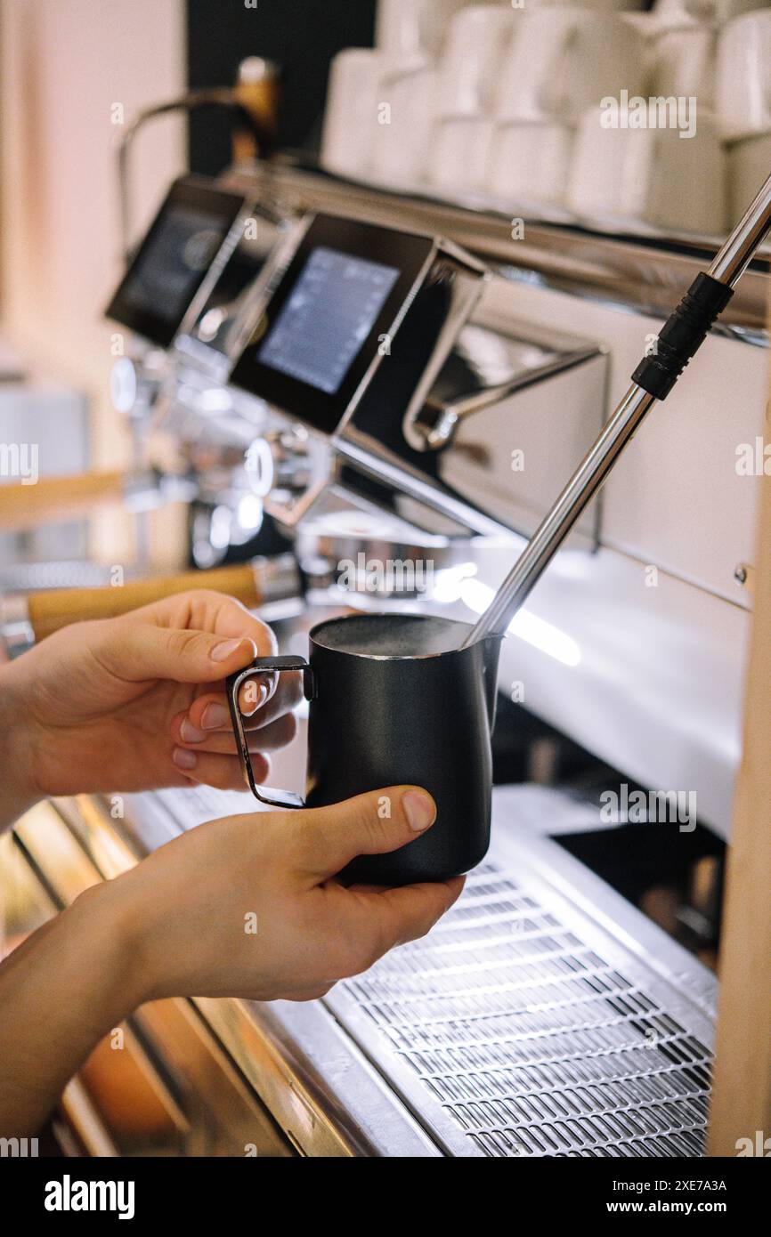 Il barista prepara la schiuma di latte nella tazza metallica Foto Stock