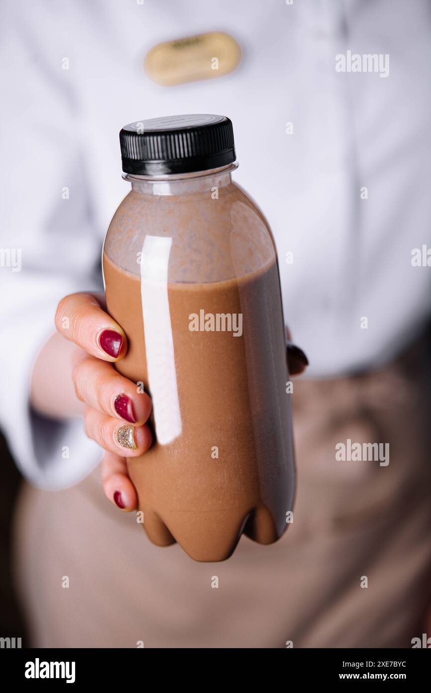Donna che tiene i frullati di cioccolato in bottiglie di plastica Foto Stock
