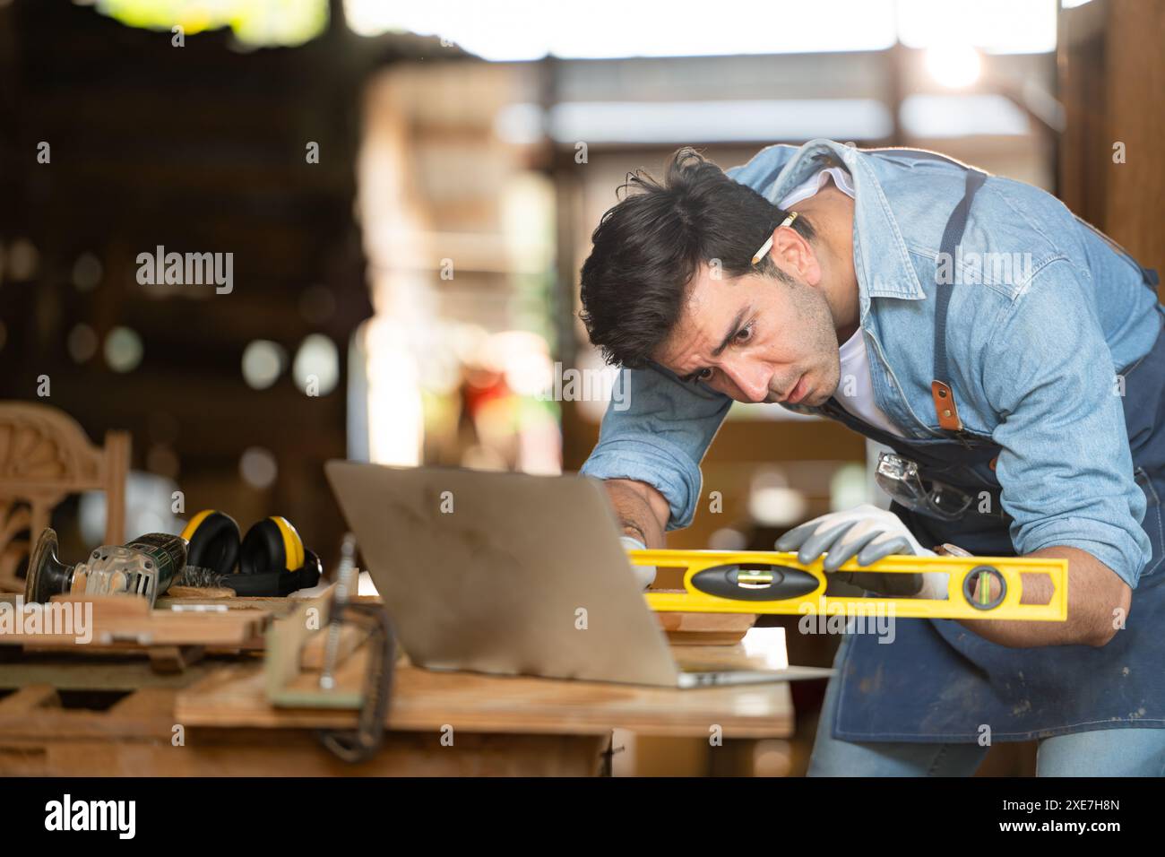 Carpentiere che lavora su un computer portatile nella sua officina in una fabbrica di lavorazione del legno Foto Stock