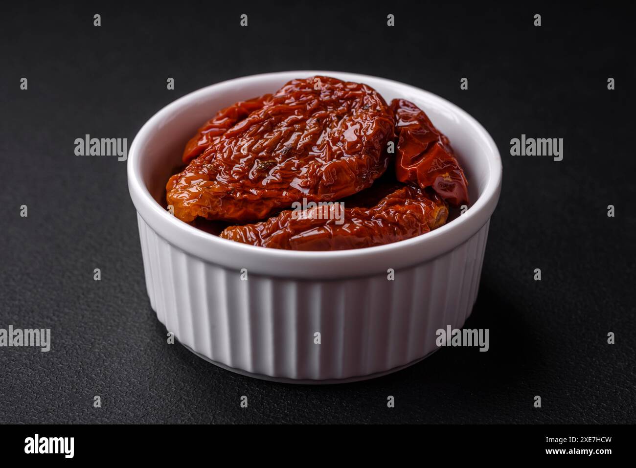 Deliziosi pomodori secchi sotto l'olio in un recipiente di ceramica bianco Foto Stock