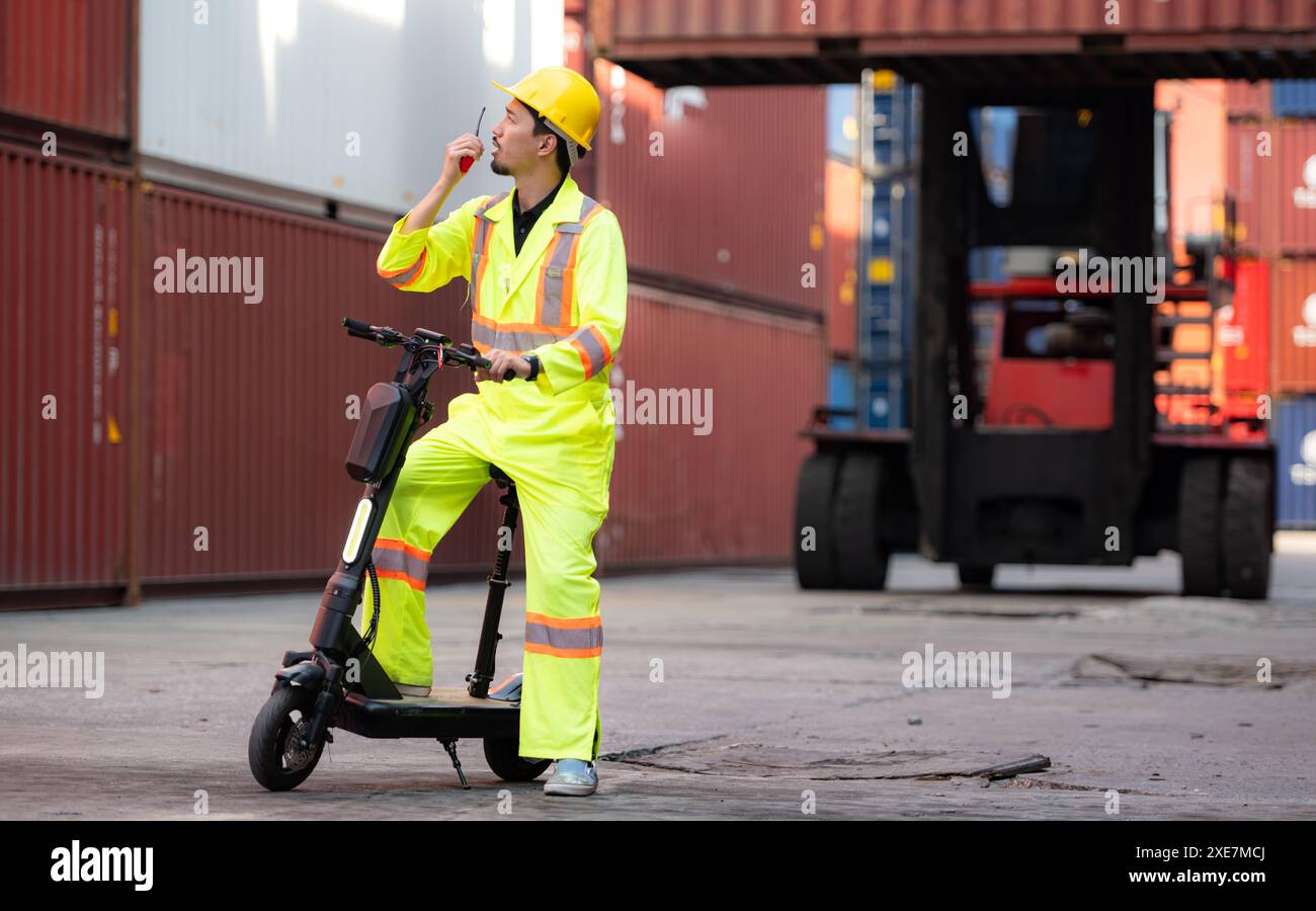 Ritratto di un magazziniere che parla su un walkie talkie con un collega in un magazzino di container vuoto mentre guida un flagello Foto Stock