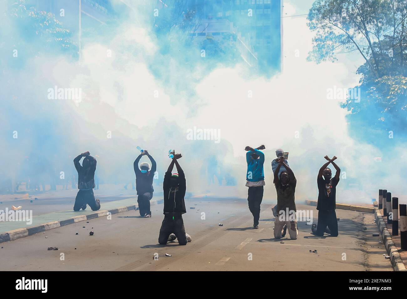 Nairobi, Kenya. 25 giugno 2024. I manifestanti si inginocchiano e si alzano le mani mentre la polizia anti-sommossa usa gas lacrimogeni per loro durante la dimostrazione. I giovani manifestanti si sono organizzati sotto la bandiera di "Occupy Parliament", coraggiosi gas lacrimogeni, cannoni ad acqua e una pesante presenza della polizia mentre marciavano per le strade della città, cantando e chiedendo ai loro leader di respingere il disegno di legge. La polizia del Kenya ha bloccato le strade che portano al parlamento e alla State House per fermare le proteste guidate dai giovani contro gli aumenti fiscali proposti nel disegno di legge finanziario del Kenya 2024/2025. Credito: SOPA Images Limited/Alamy Live News Foto Stock