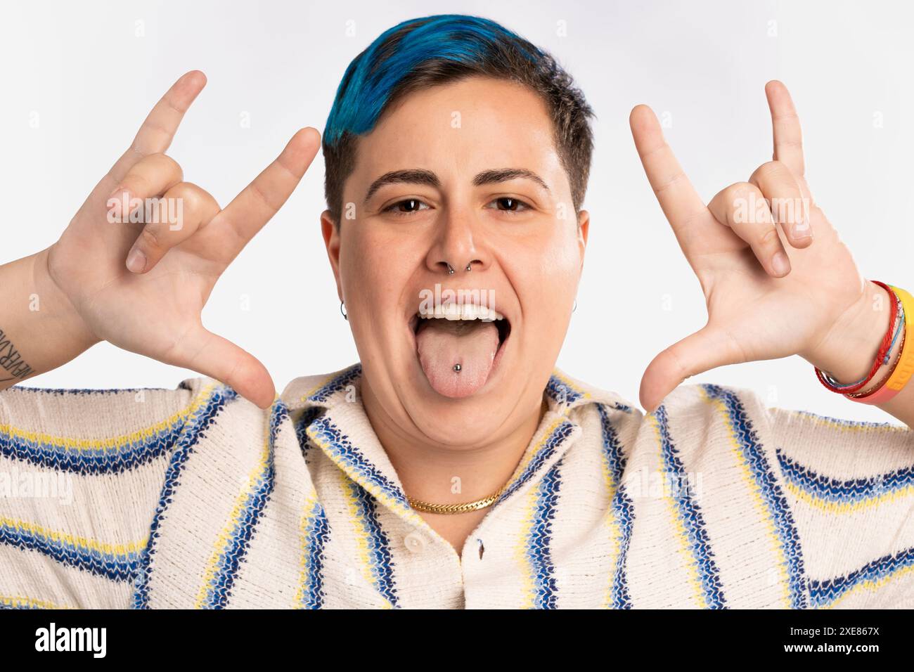 Persona giocosa androgina con i capelli blu che sporgono la lingua mostrando piercing - braccialetto orgoglio LGBT, espressione gioiosa, divertente e vibrante - incluso a. Foto Stock