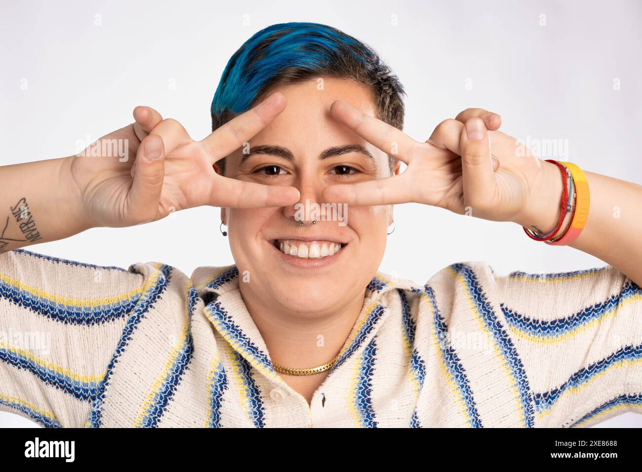 Persona androgina sorridente con capelli blu che fa un gesto giocoso della mano - braccialetto orgoglio LGBT, espressione felice, inclusivo e divertente - vibrante e colorato Foto Stock