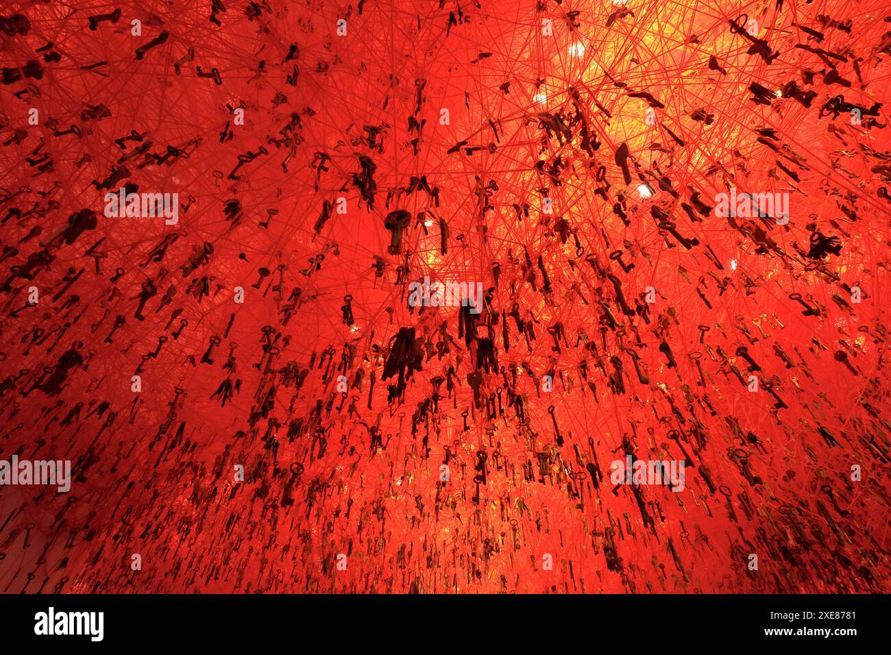 Molti tasti appesi al soffitto in un'installazione artistica astratta illuminata in rosso Foto Stock