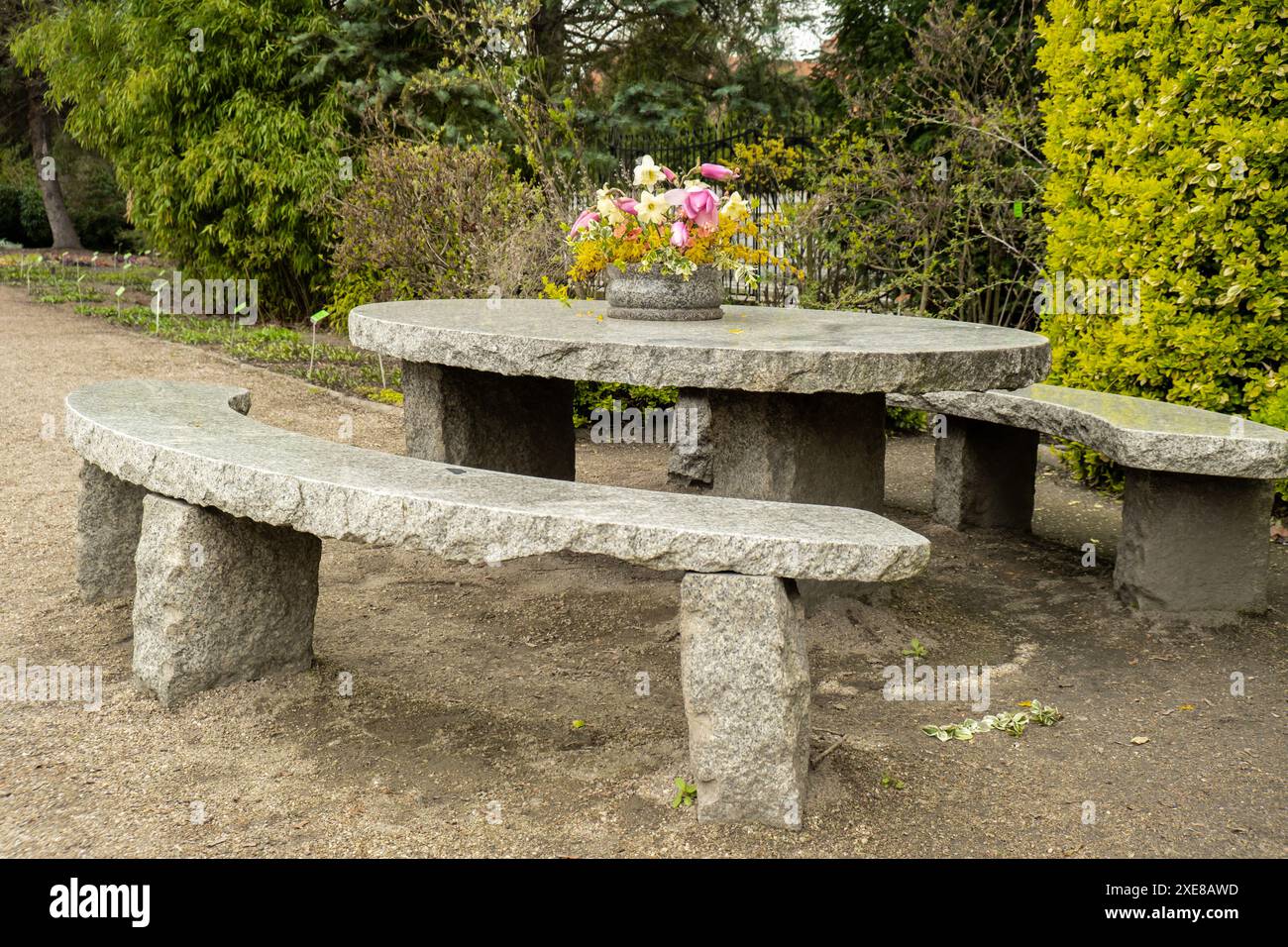 Grande tavolo rotondo in pietra su una splendida terrazza e giardino con patio. Posto vuoto per rilassarsi all'aperto nel cortile. Fiori vintage in vaso. Co Foto Stock