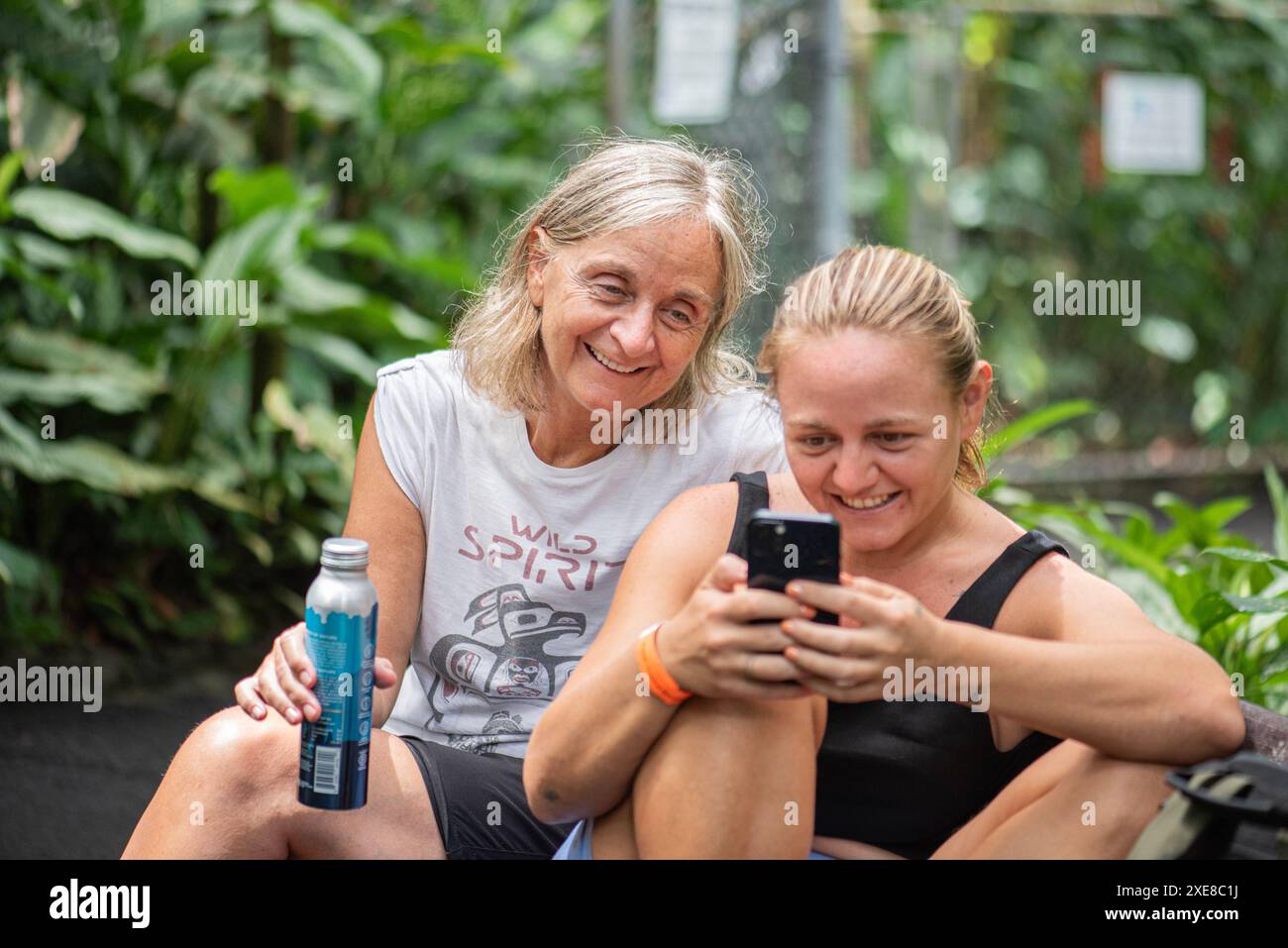 Nella tranquilla cornice del giardino botanico Hilo alle Hawaii, una madre e sua figlia sono seduti insieme, sorridendo gioiosamente mentre guardano attraverso il fotogr Foto Stock