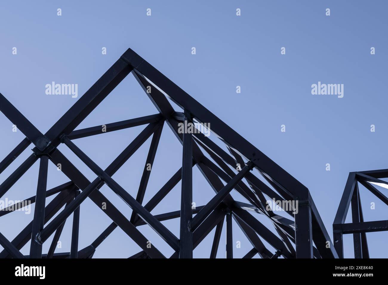 Scena urbana con composizione geometrica di travi metalliche rosse e una gru blu in una costruzione moderna contro un cielo azzurro. Foto Stock