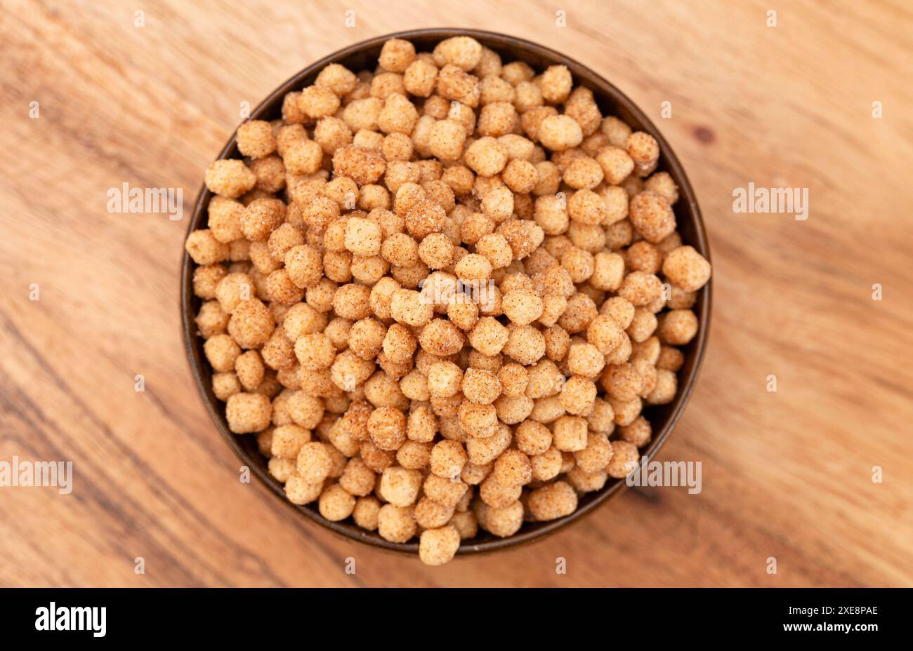 Ciotola di piccolo pane tostato alla cannella a forma di palla e cereali da colazione su un tavolo da cucina in legno Foto Stock