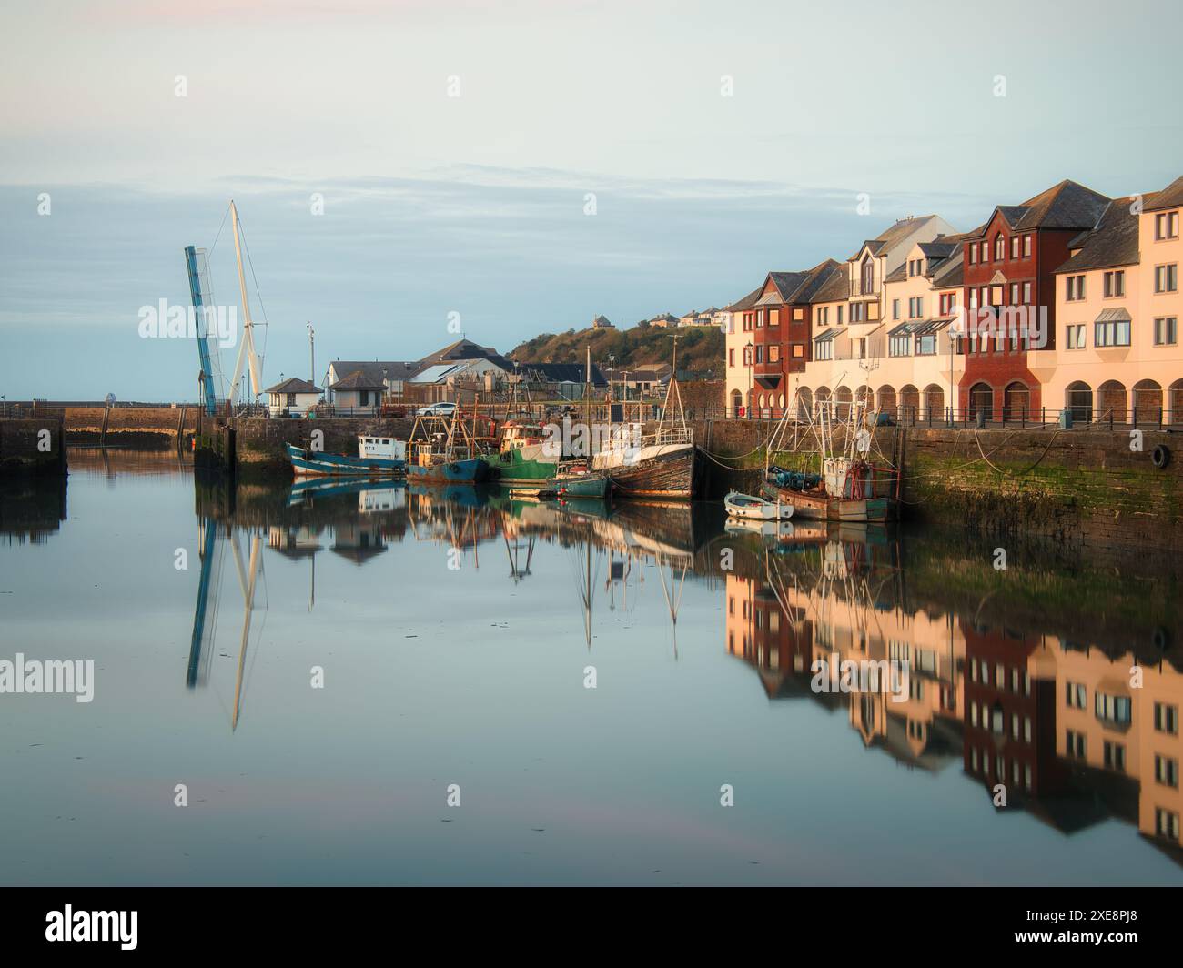 Mentre il crepuscolo inizia a cadere sull'antico porto di Maryport, i mari calmi fungono da specchio per le barche da pesca in funzione Foto Stock