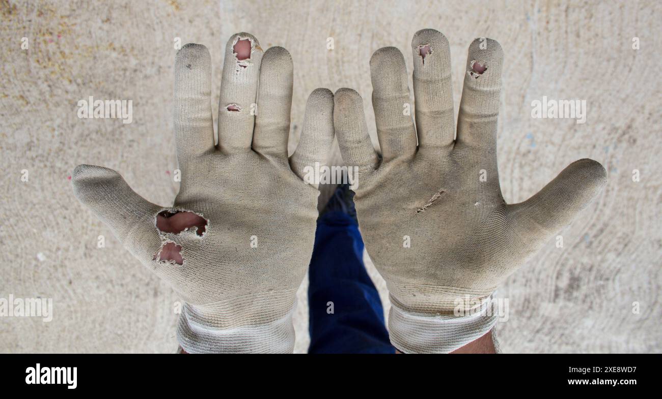 Immagine delle mani di un operaio edile con guanti da lavoro strappati. Riferimento a un lavoro faticoso Foto Stock