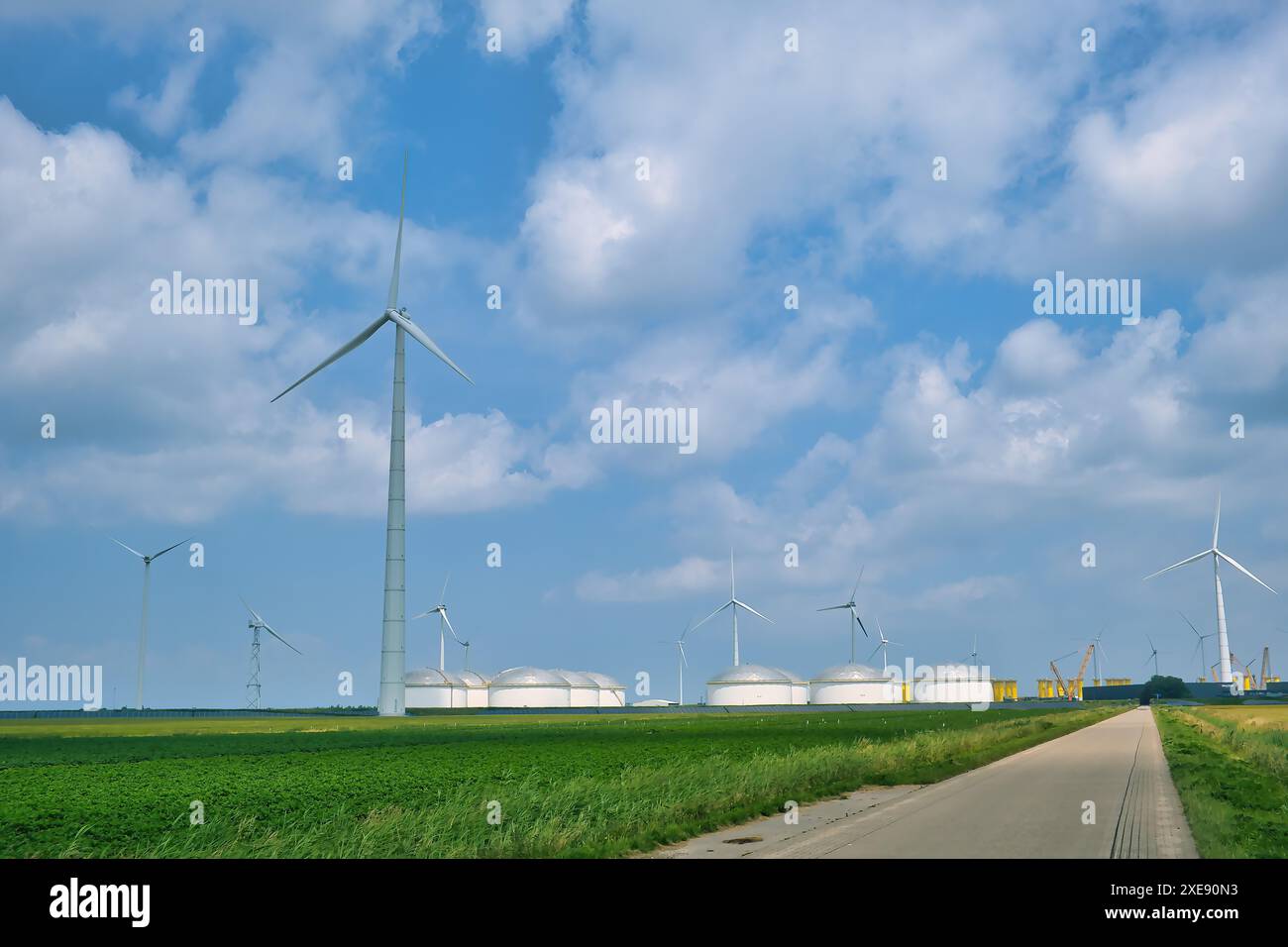 Strada che conduce a grandi turbine eoliche e serbatoi di stoccaggio del petrolio nella zona industriale di Eemshaven, provincia di Groningen, Paesi Bassi. Foto Stock