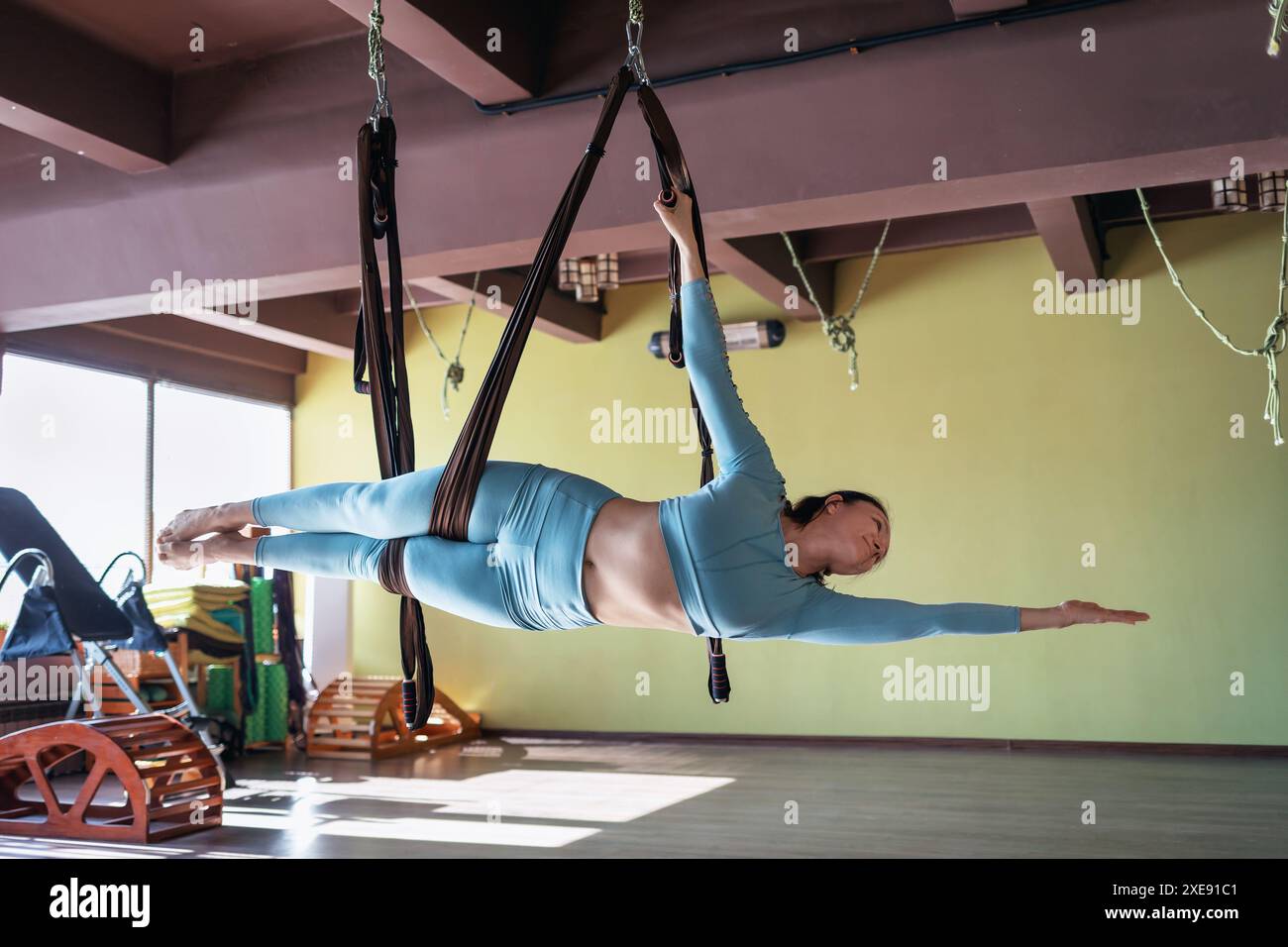 Una donna di aspetto europeo, che fa yoga aereo in palestra, esegue l'esercizio Vasishthasana, posa su una tavola laterale in un'amaca, si allena da sola in S. Foto Stock