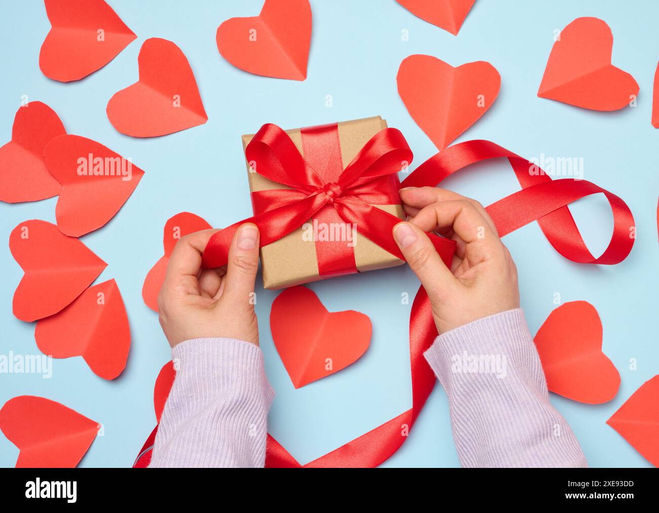 La mano di una donna regge una confezione regalo avvolta da un nastro di seta rosso su sfondo blu Foto Stock